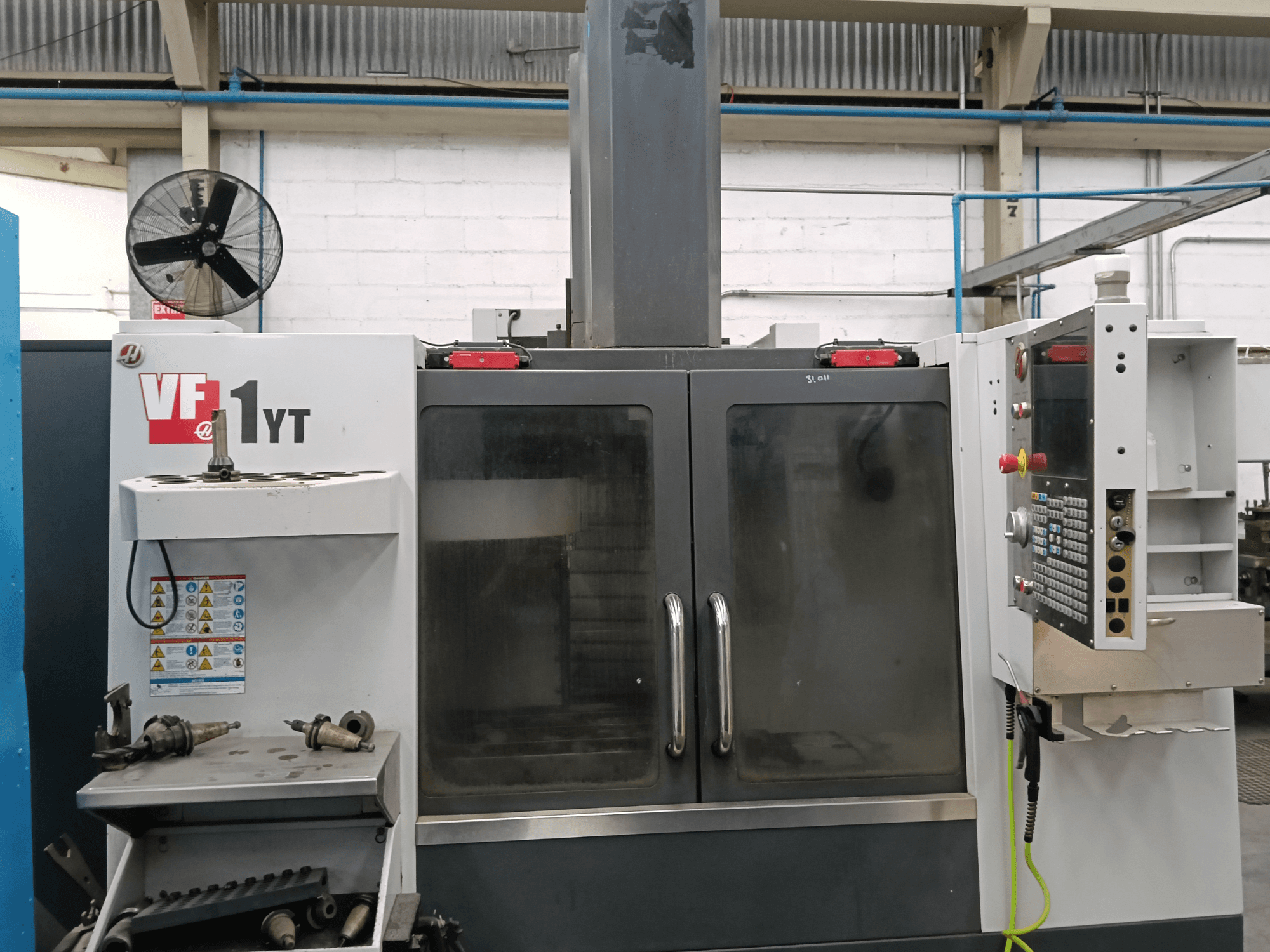 HAAS VF-1YT-1 dikey işleme merkezinin, yan tarafında kontrol paneli ve takımların bulunduğu önden görünümü.