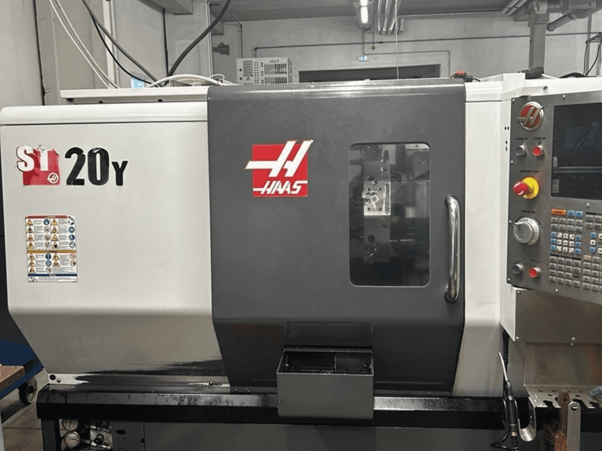Haas ST-20Y CNC torna tezgahı, önden görünüm, kontrol panelini, güvenlik etiketlerini ve çalışma penceresini gösterir.