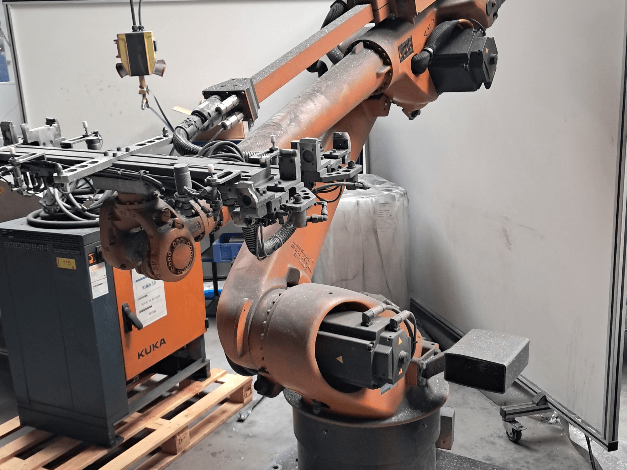 KUKA KR 30L16-2 robot kolunun yandan görünümü; karmaşık uç efektör ve kontrol kabloları ile birlikte, bir KUKA kontrol kutusunun yanında yer almaktadır.
