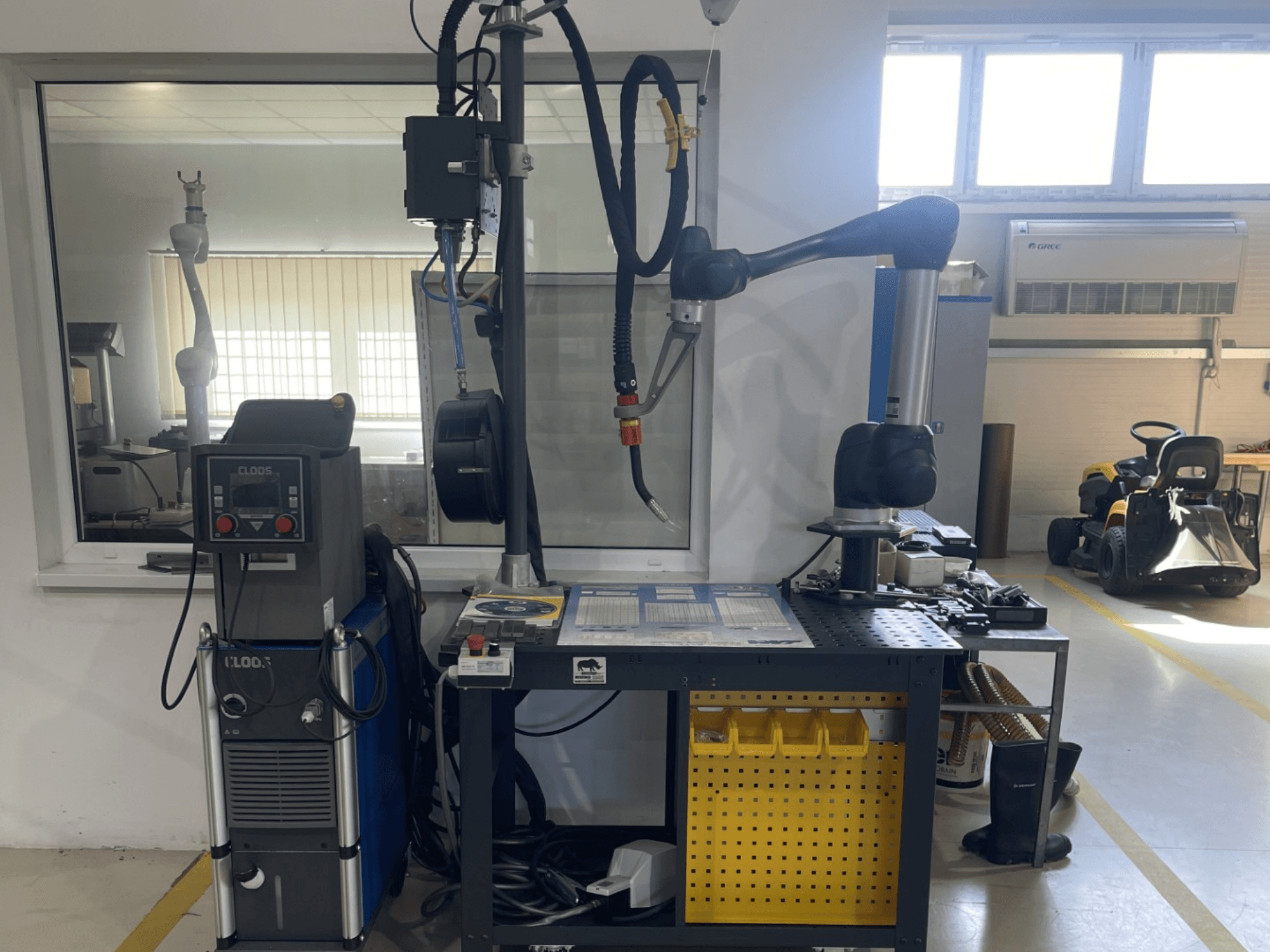 Bir atölyede bulunan DOOSAN M1013 işbirlikçi robot; çalışma tezgahı üzerinde kaynak ekipmanı ve aletlerin bulunduğu yan görünüm.