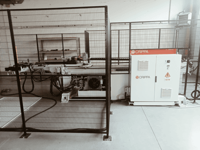 Bir güvenlik kafesinin arkasında, hortumları ve bileşenleri görünen beyaz CRIPPA makinesi, yandan görünüm, endüstriyel ortam.