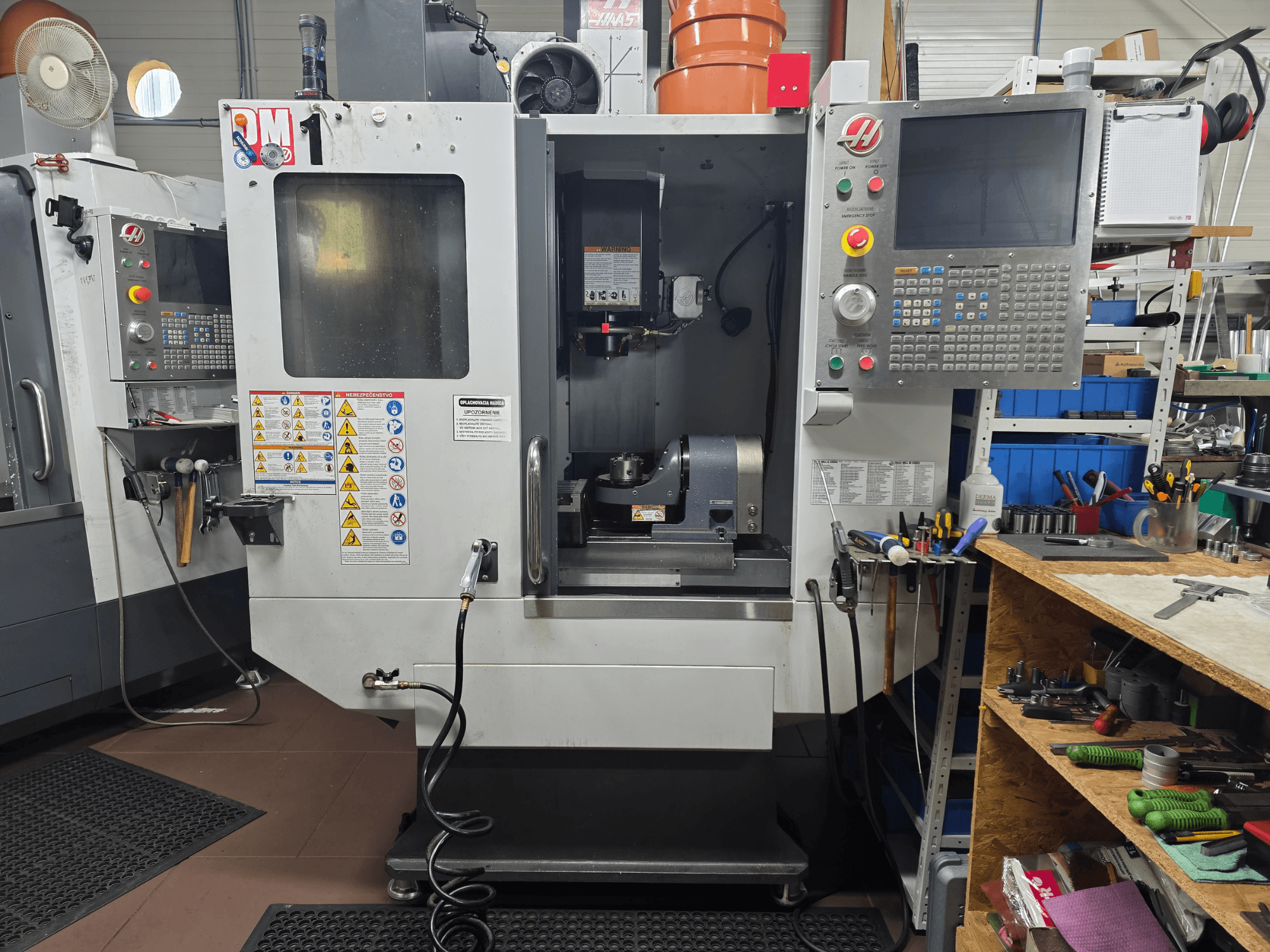 Haas CNC makine modeli VF-2, önden görünüm, kontrolleri, iş mili alanını, güvenlik etiketlerini ve yakındaki bir tezgah üzerindeki aletleri gösteriyor.