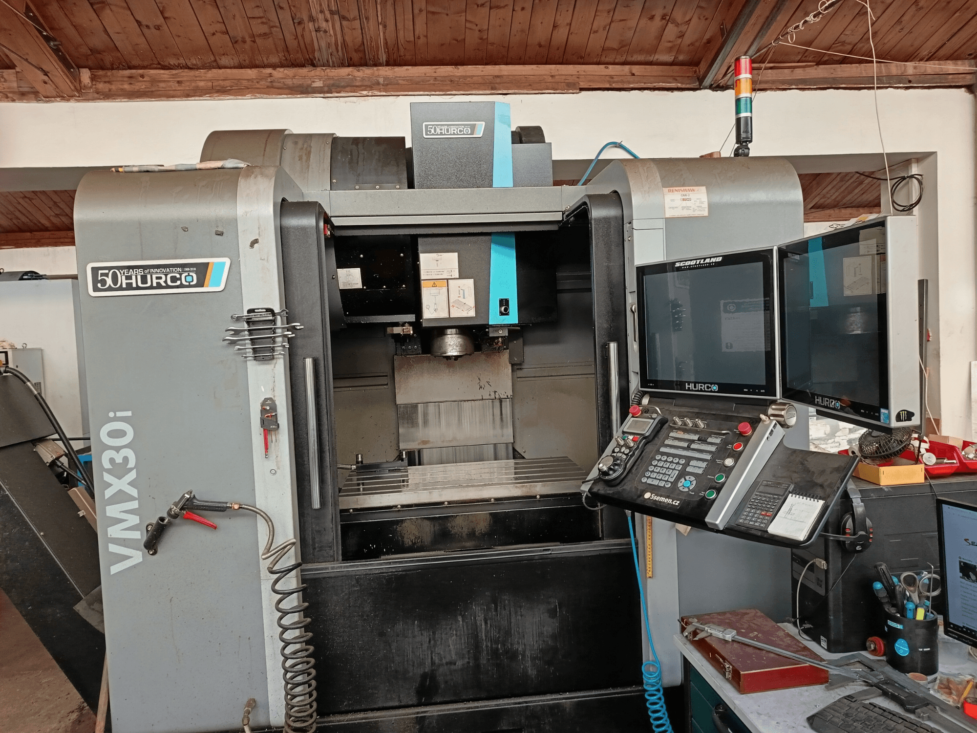 Hurco VMX30i CNC freze makinesinin önden görünümü, çift monitör, kontrol paneli ve bir hortum takılı.