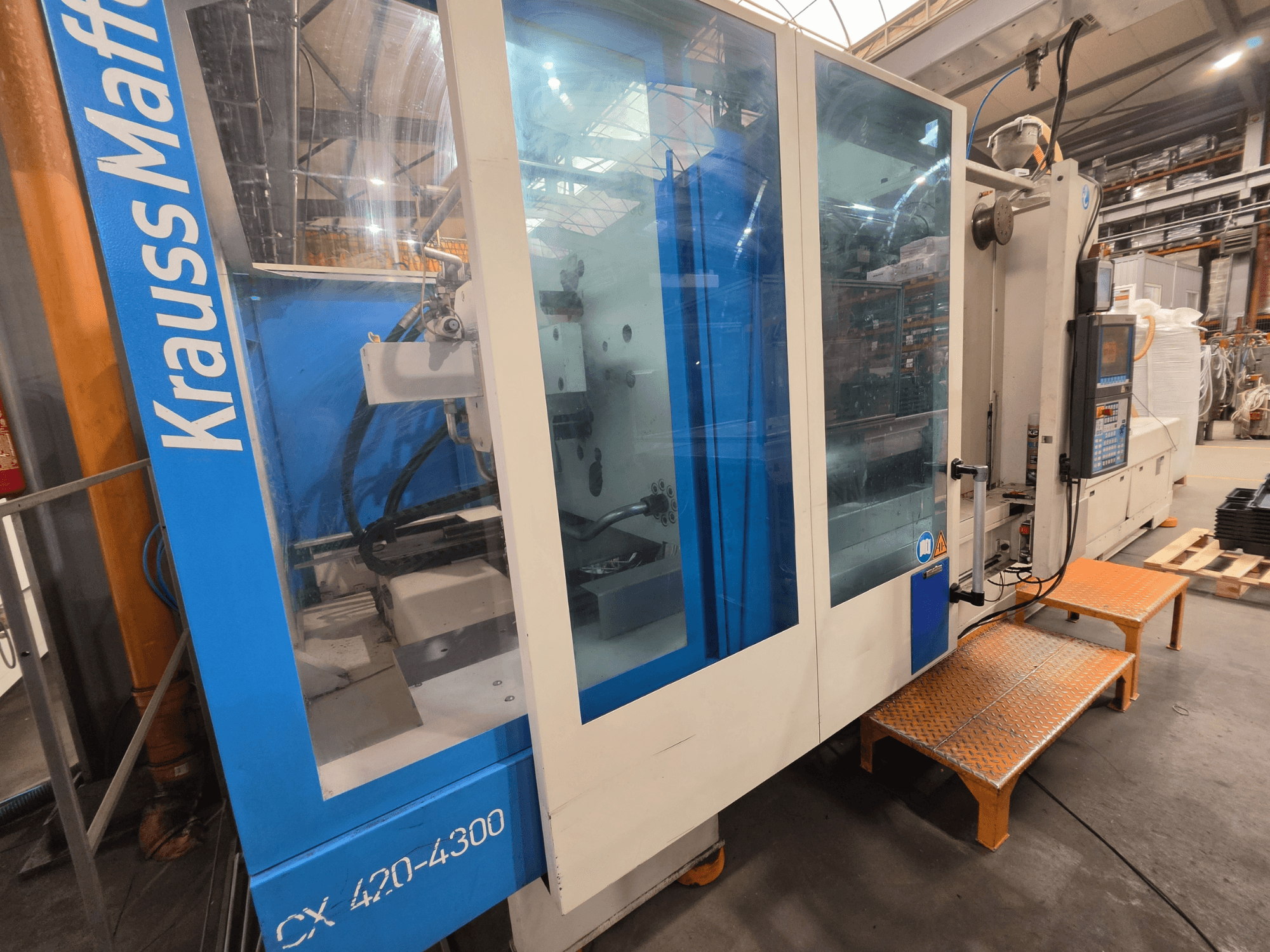 Krauss Maffei CX 420-4300 hidrolik enjeksiyon kalıplama makinesi, yandan görünüm, kontrol paneli ve şeffaf paneller.
