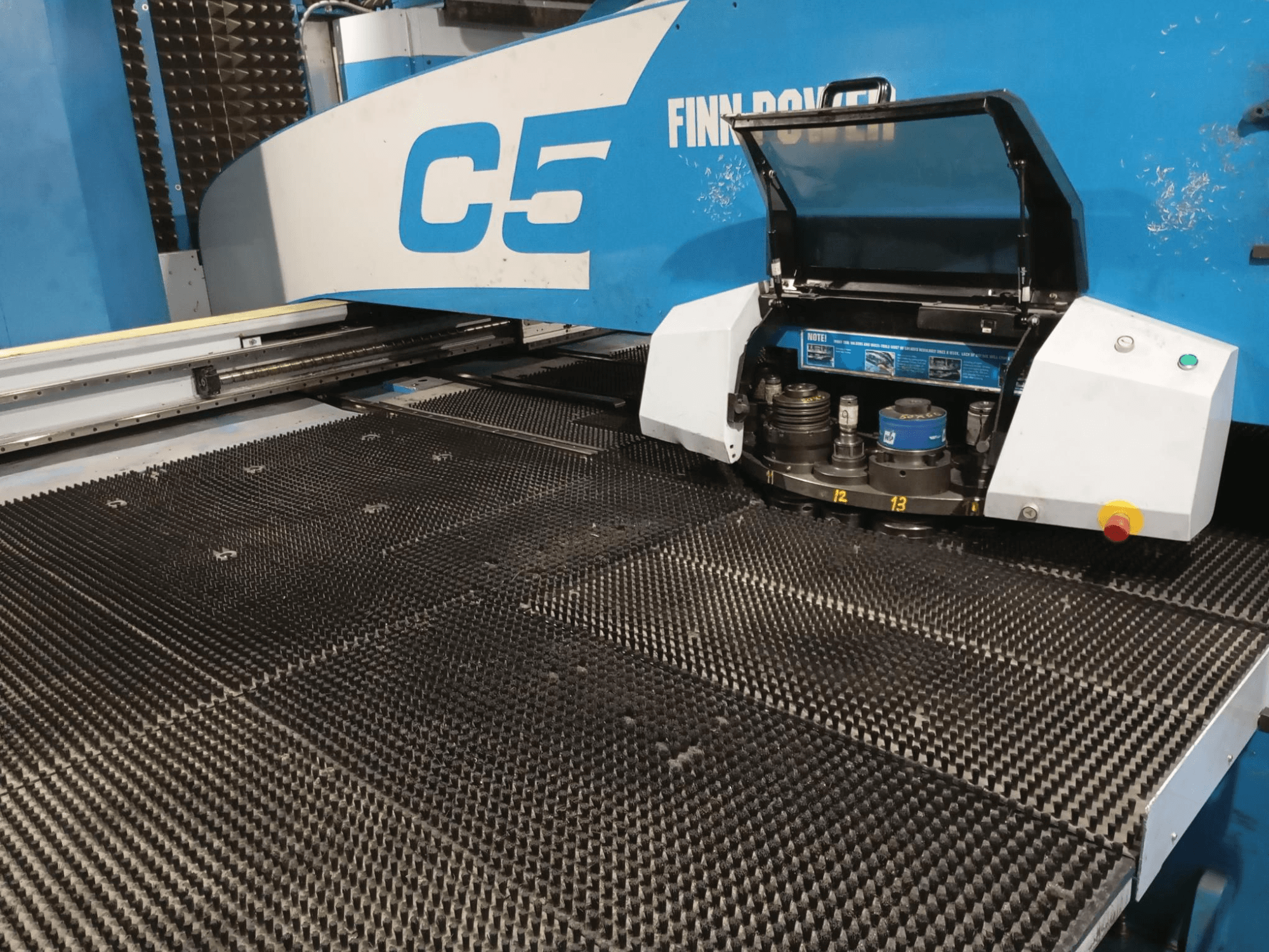 Finn-Power C5 zımba presi, önden görünüm, takım kafasını numaralandırılmış indeksleme noktalarına sahip dokulu bir çalışma masası üzerinde açık olarak göstermektedir.