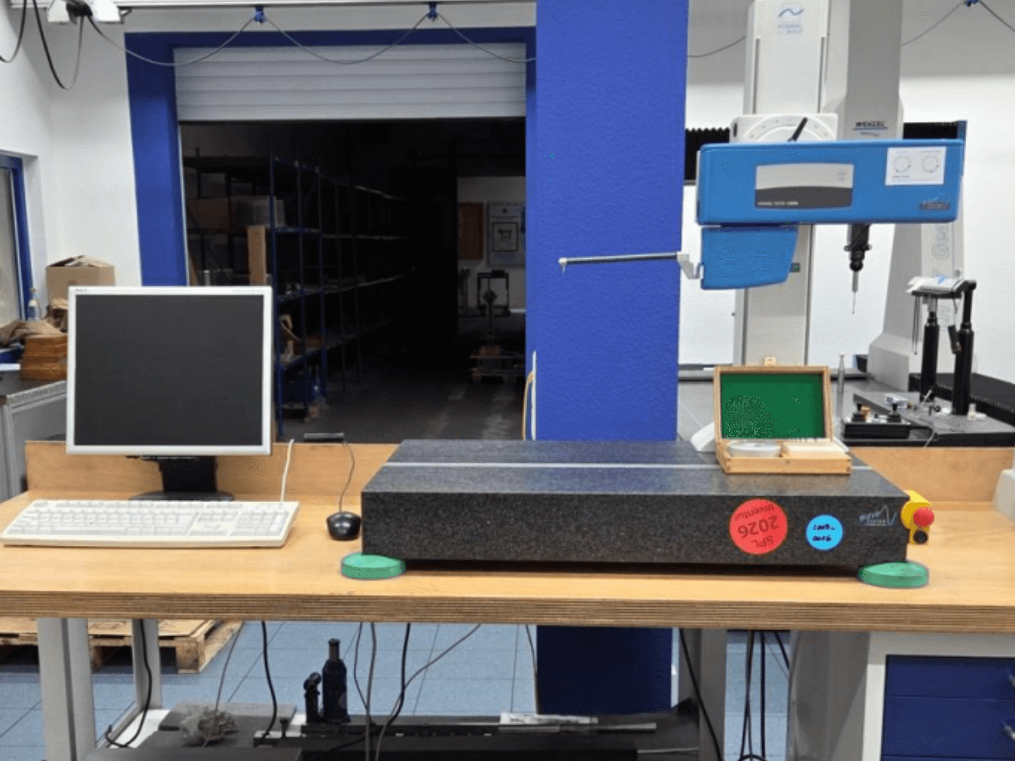 JENOPTIK wave C8000 CMM bir atölyede, monitör, klavye ve granit ölçüm yüzeyi ile birlikte. Önden görünüm.