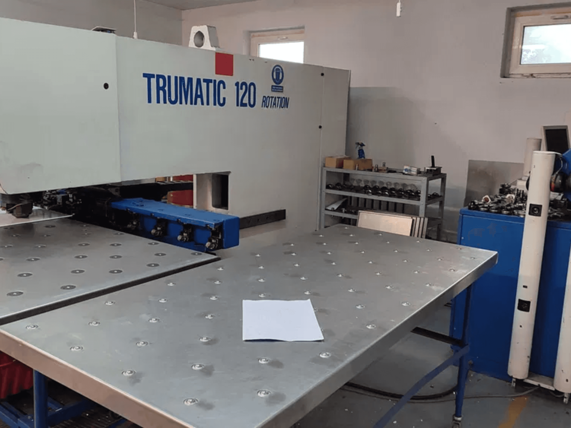 TRUMPF TRUMATIC 120R CNC zımbalama makinesi, delikli metalik bir tabla ve boş bir levha ile önden görülüyor.