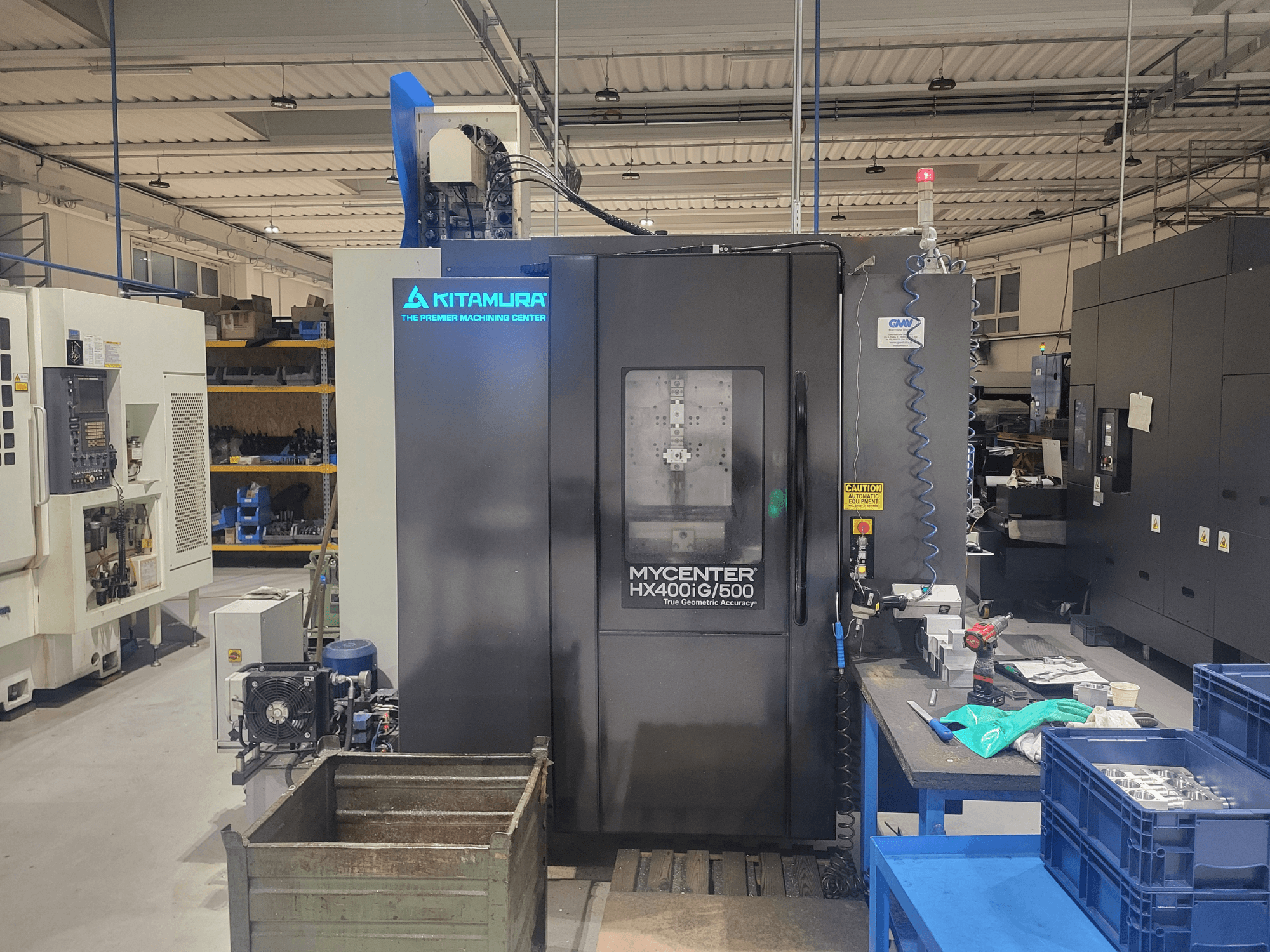 Kitamura Mycenter HX400iG/500 CNC makinesi bir atölyede, önden görünüm, kontroller, takım deposu ve malzemeler yakında.