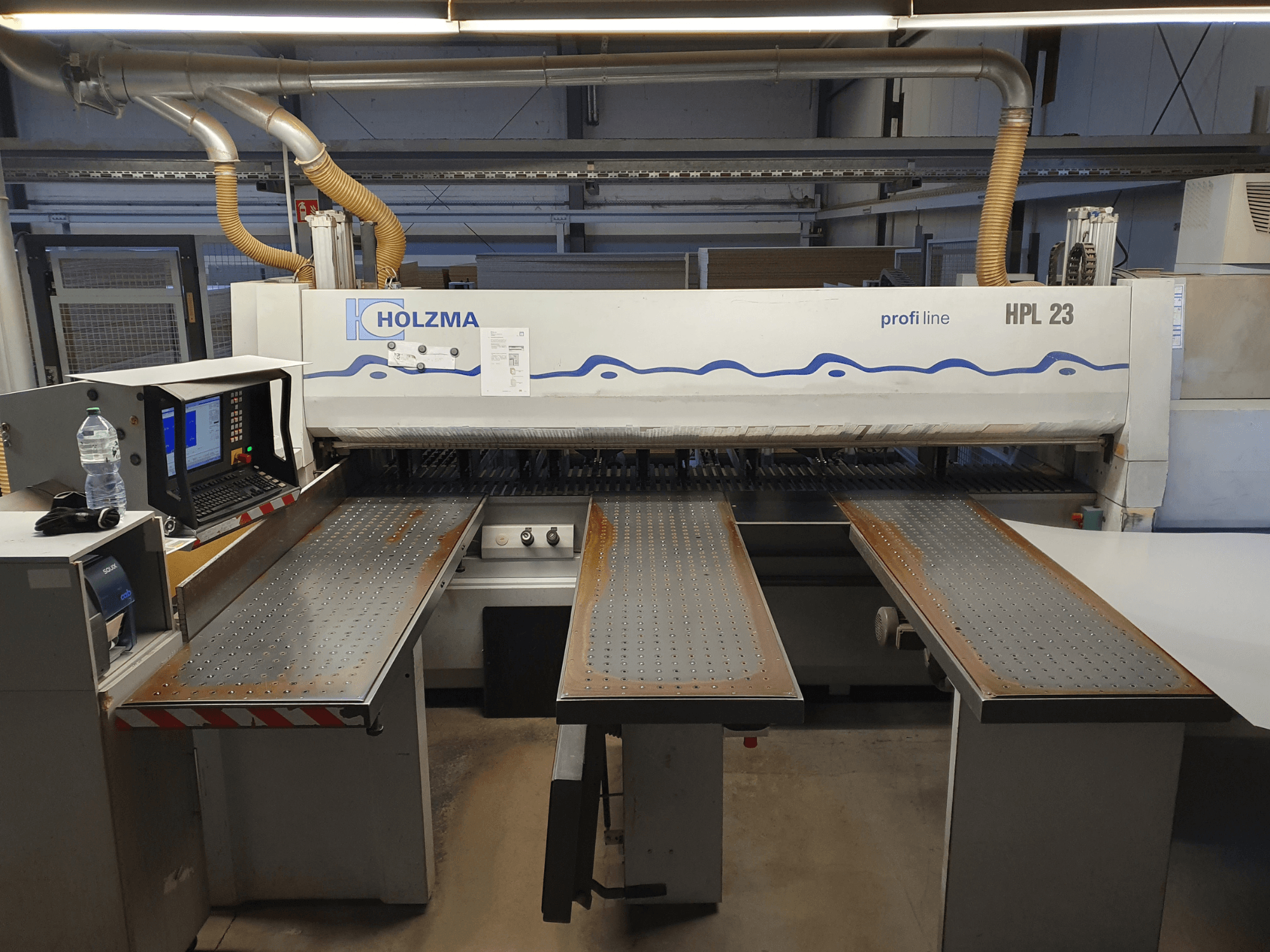 HOLZMA HPL 23 kesme makinesi, üç delikli tabla, bilgisayar terminali ve yanında su şişesi ile önden gösterilmiştir.