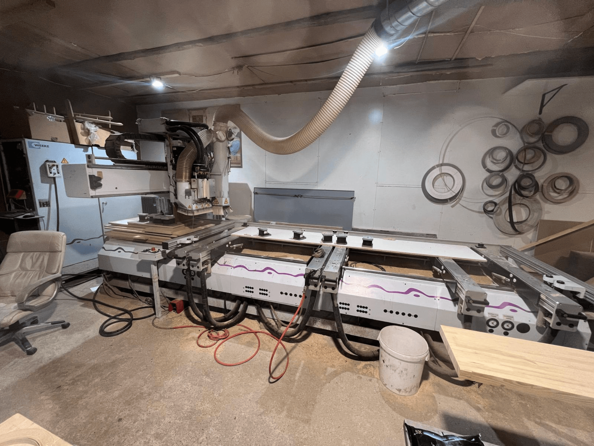 Atölyede bulunan Weeke OPTIMAT BP 120 CNC Ahşap İşleme Merkezi; ön görünümde, yüzeyde ahşap parçaları ve aletler görülüyor.