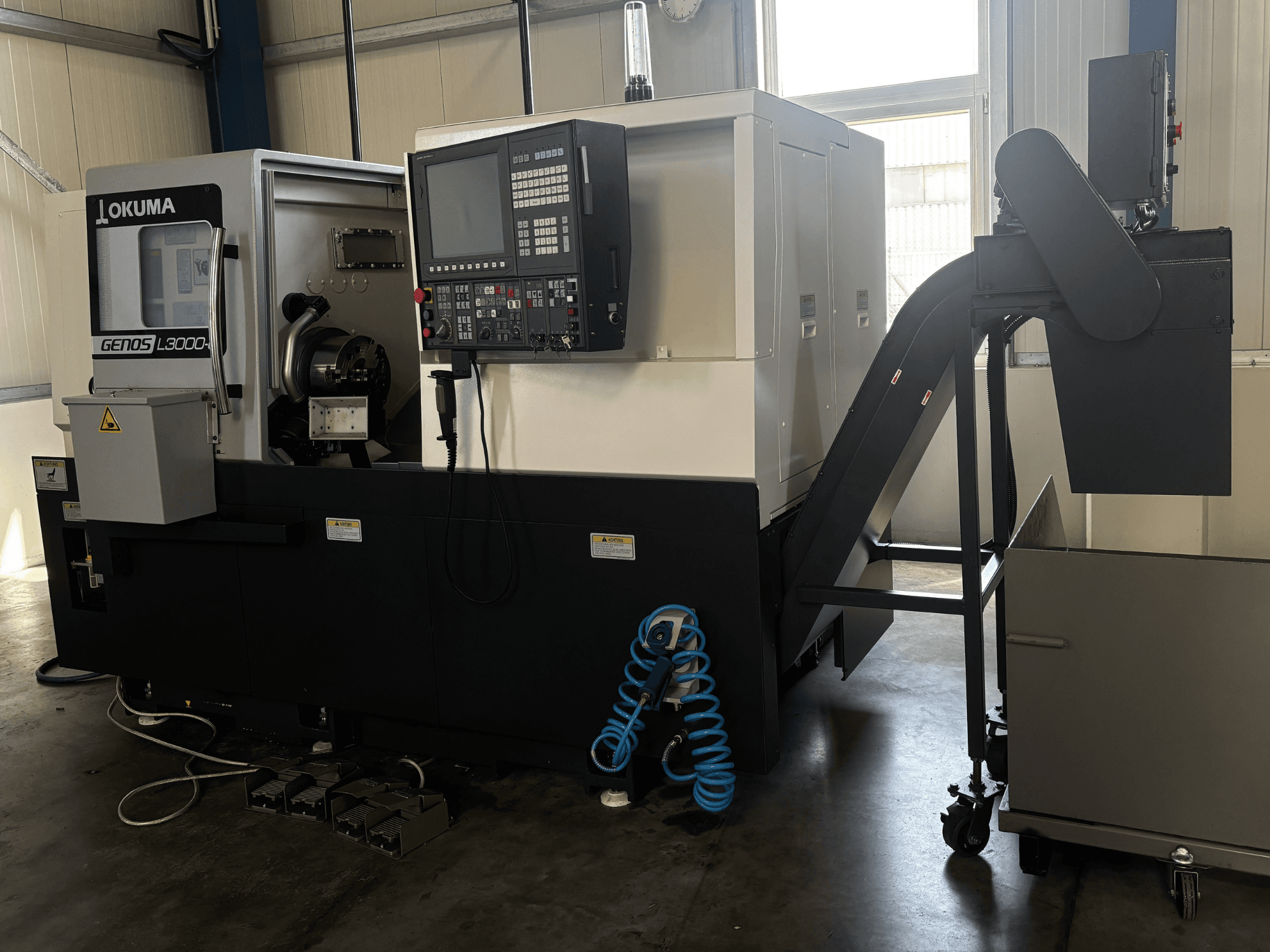 Okuma GENOS L3000-e yatay torna tezgahı, önden görünüm; kontrol paneli, konveyör ve iş mili bölümü görülmektedir.