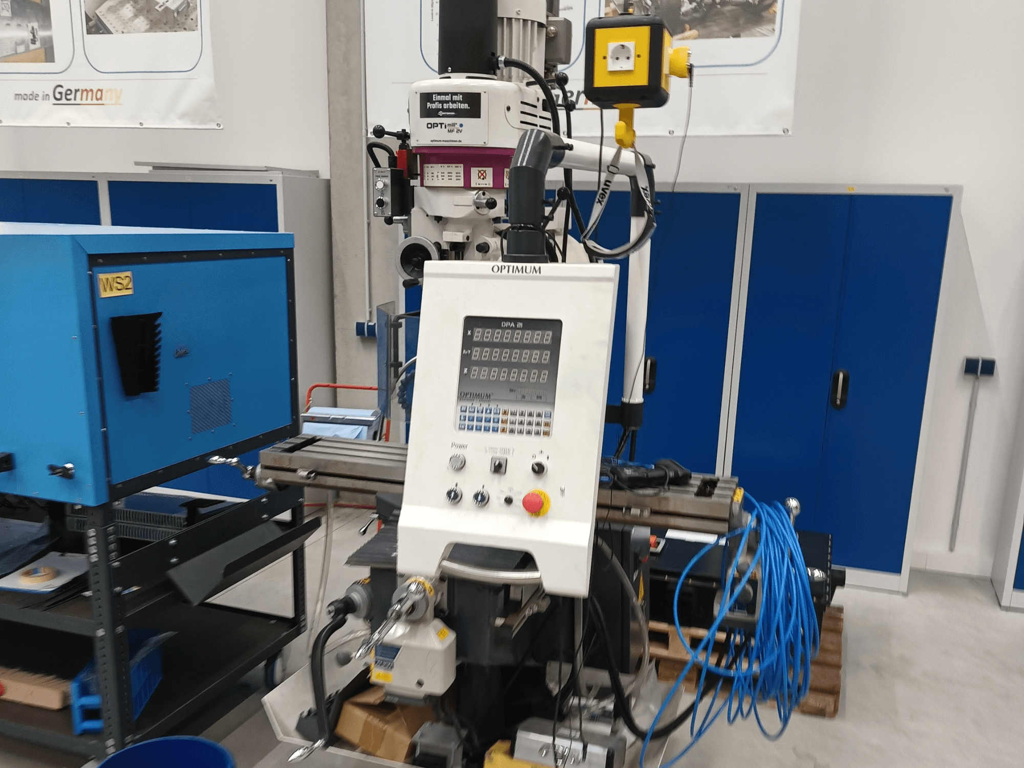 Optimum OPTImill MF 2V dikey işleme merkezi; kontrol paneli, iş mili ve mavi destek arabasını gösteren önden görünüm.