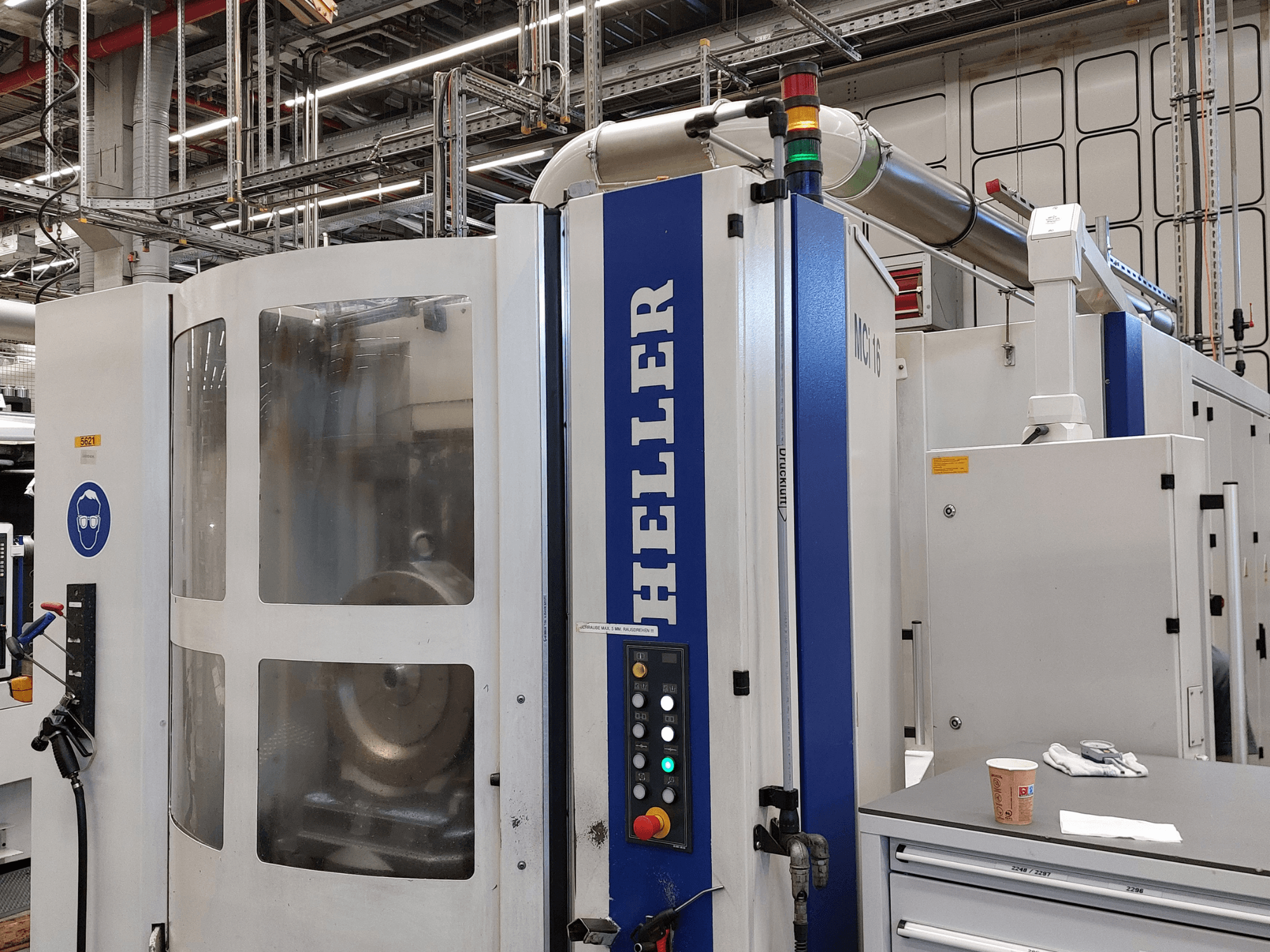 Fabrika ortamında, kontrol paneli ve güvenlik işaretleriyle donatılmış Heller MCI 16 dikey işleme merkezi.