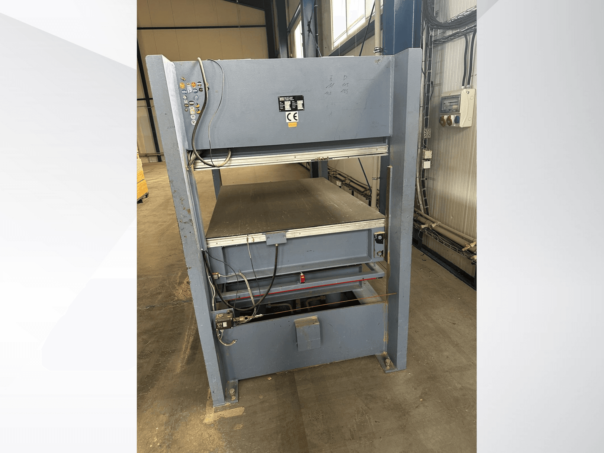 Önden bakıldığında kontrol panelli gri endüstriyel makine; ayarlanabilir platformlar ve güvenlik işaretleri içerir.