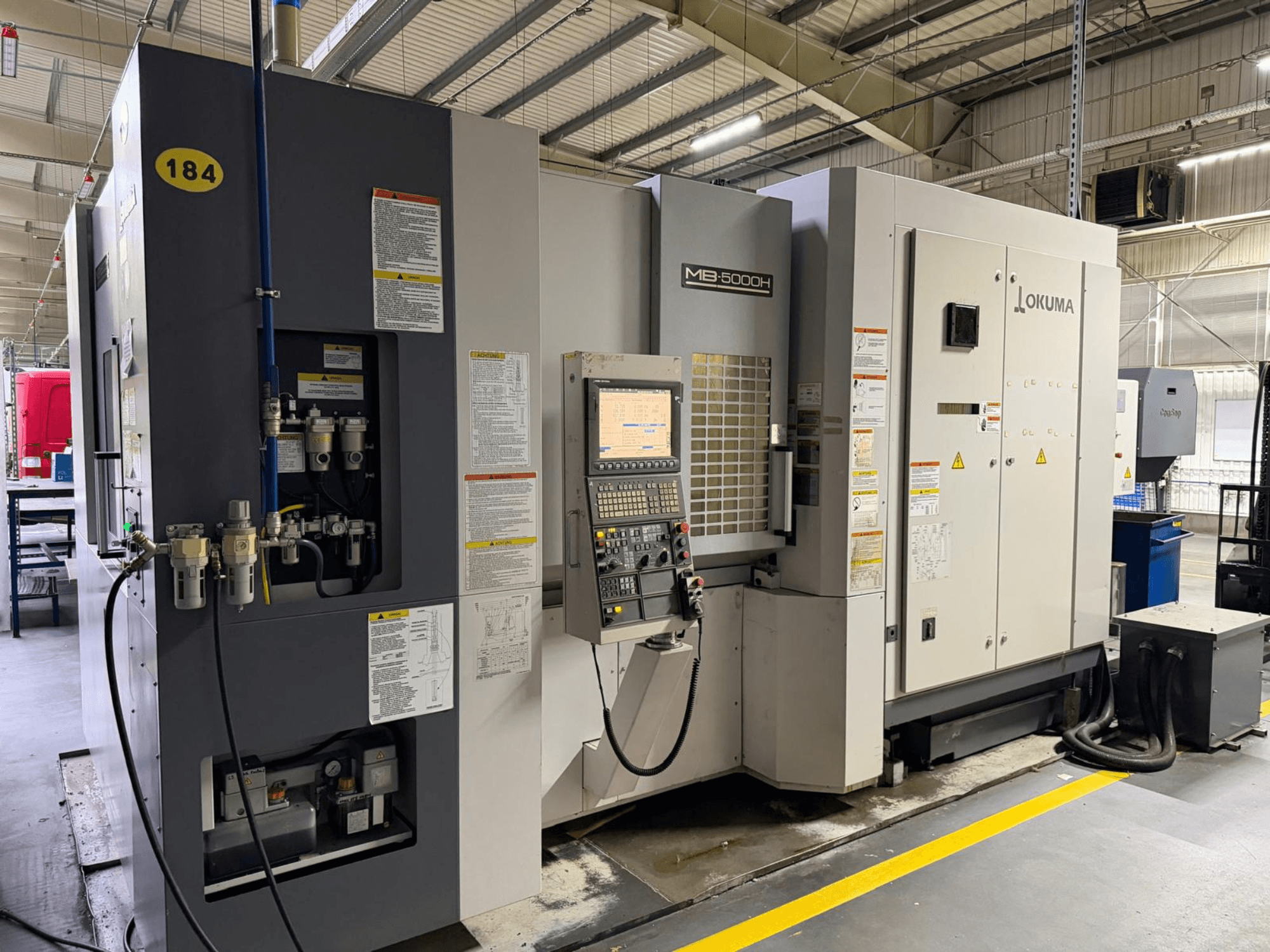 Okuma MB 5000H yatay işleme merkezi önden görünüm, kontroller, etiketleme ve hidrolik bağlantılar.