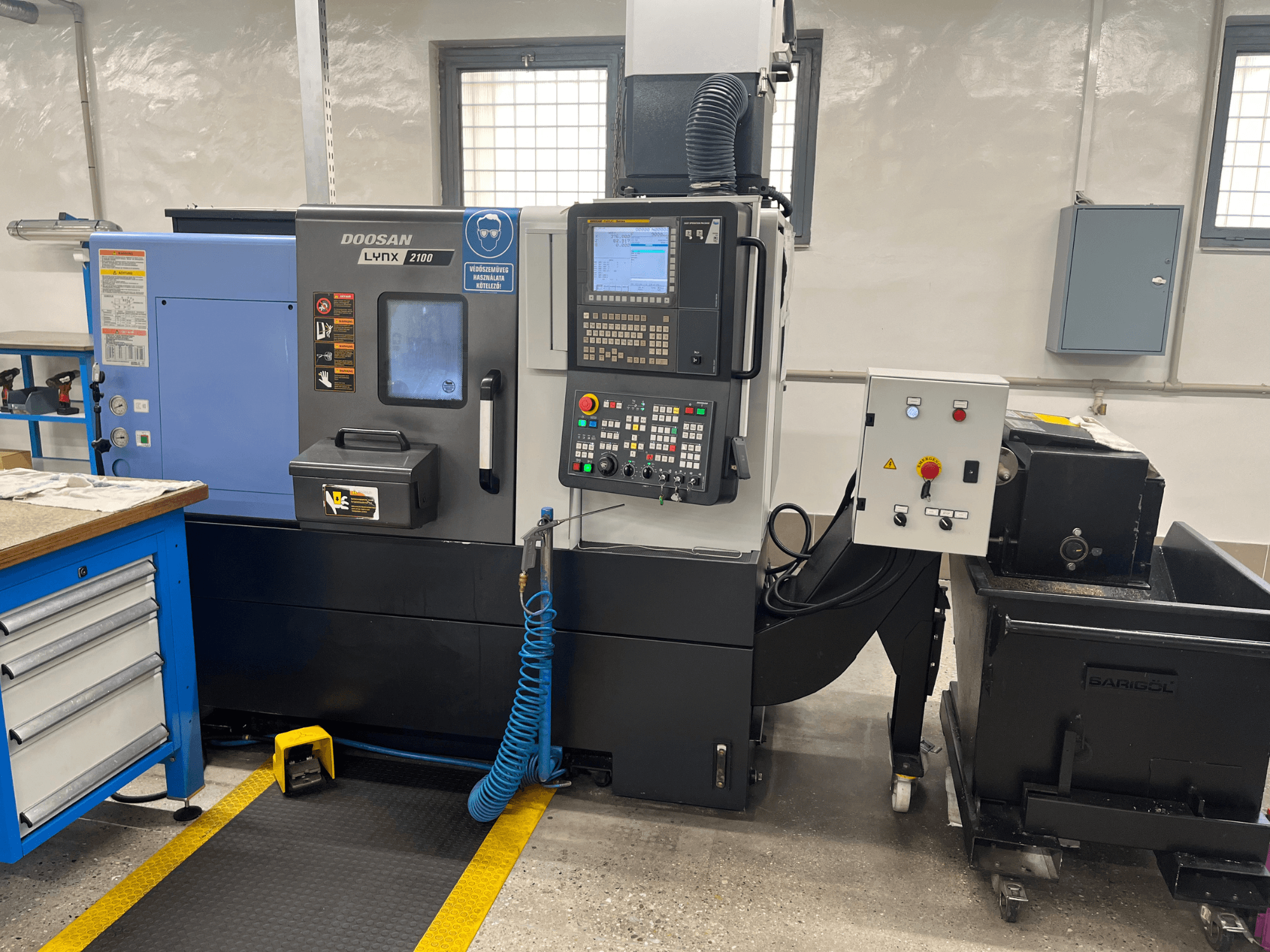 Atölyede Doosan Lynx 210 torna tezgahı, kontrol paneli, takım depolama ve soğutma sistemi, çalışma alanı detayları ile yandan görünüm.