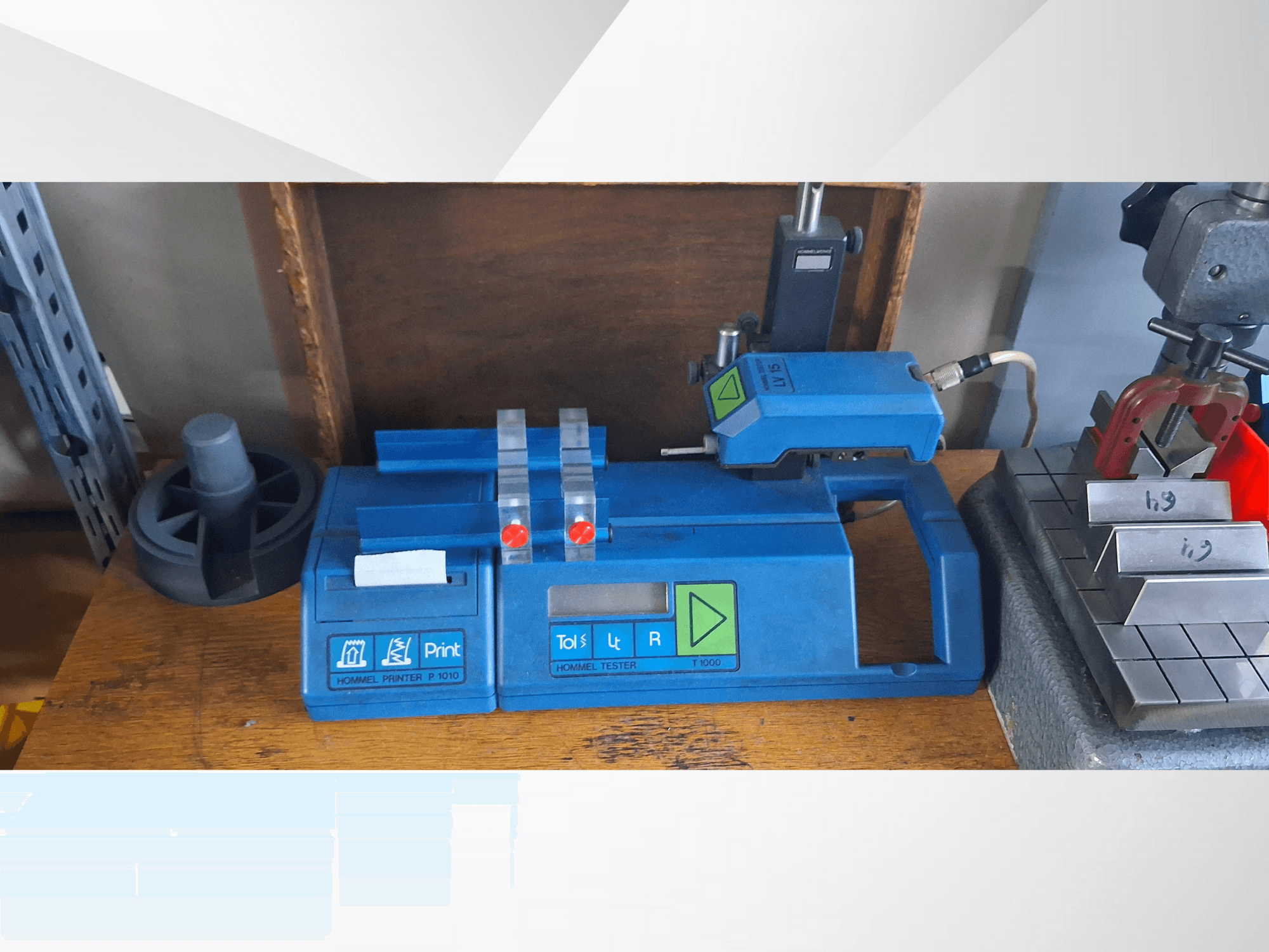 Mavi Hommel T 1000 yazıcı ve kırmızı düğmeli T 1 010 test cihazı, metal bloklu bir tezgah üzerinde önden görülüyor.