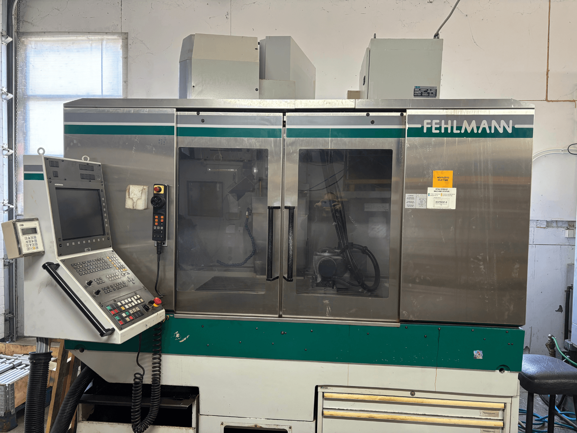 FEHLMANN Picomax 90-M dikey işleme merkezinin önden görünümü; kontrol paneli, şeffaf muhafaza ve çalıştırma düğmeleri görülmektedir.
