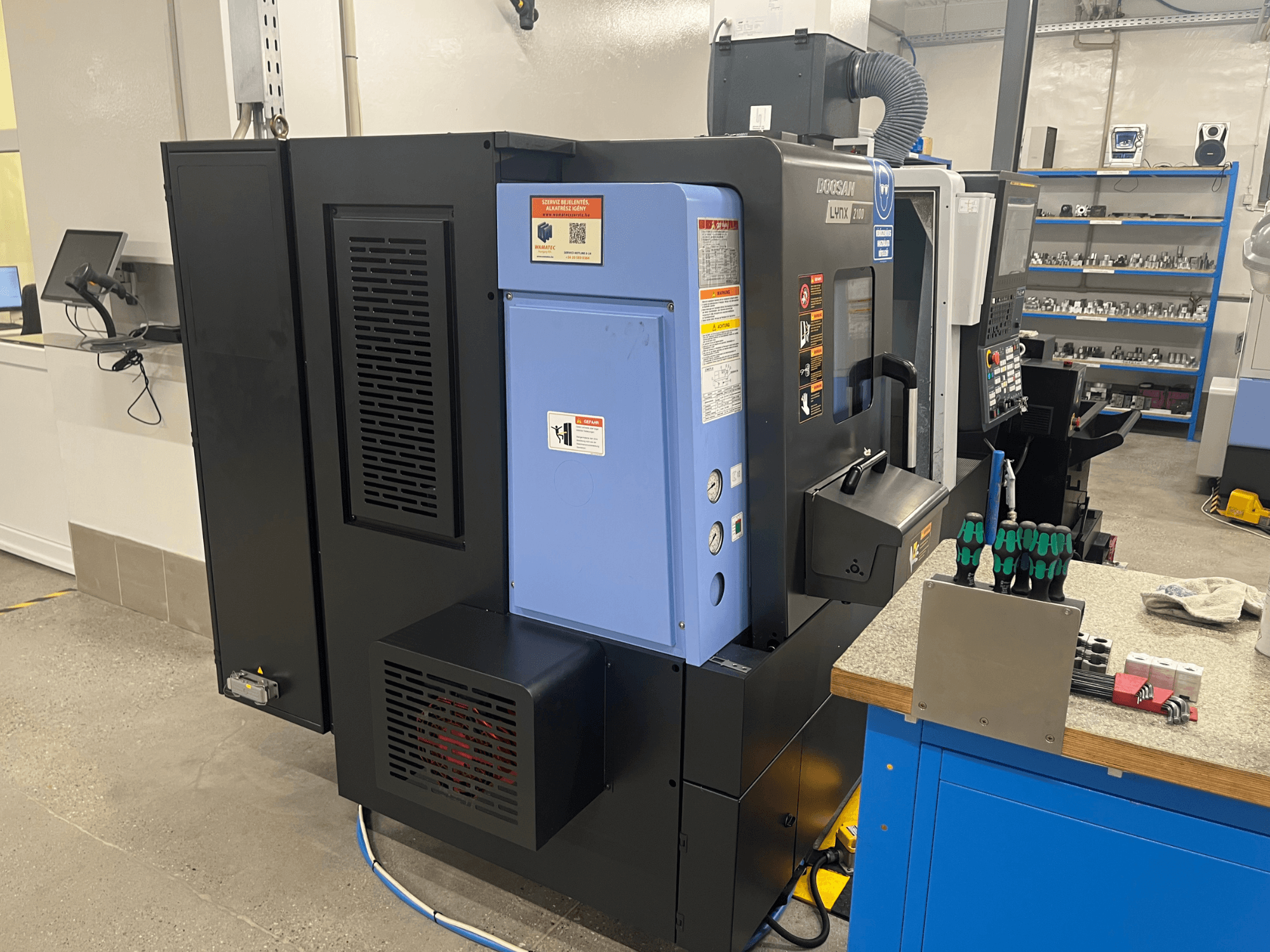 Doosan Lynx 2100 torna tezgahı, yandan görünüm, kontrol paneli, havalandırma sistemi ve tezgah üzerindeki aletler.