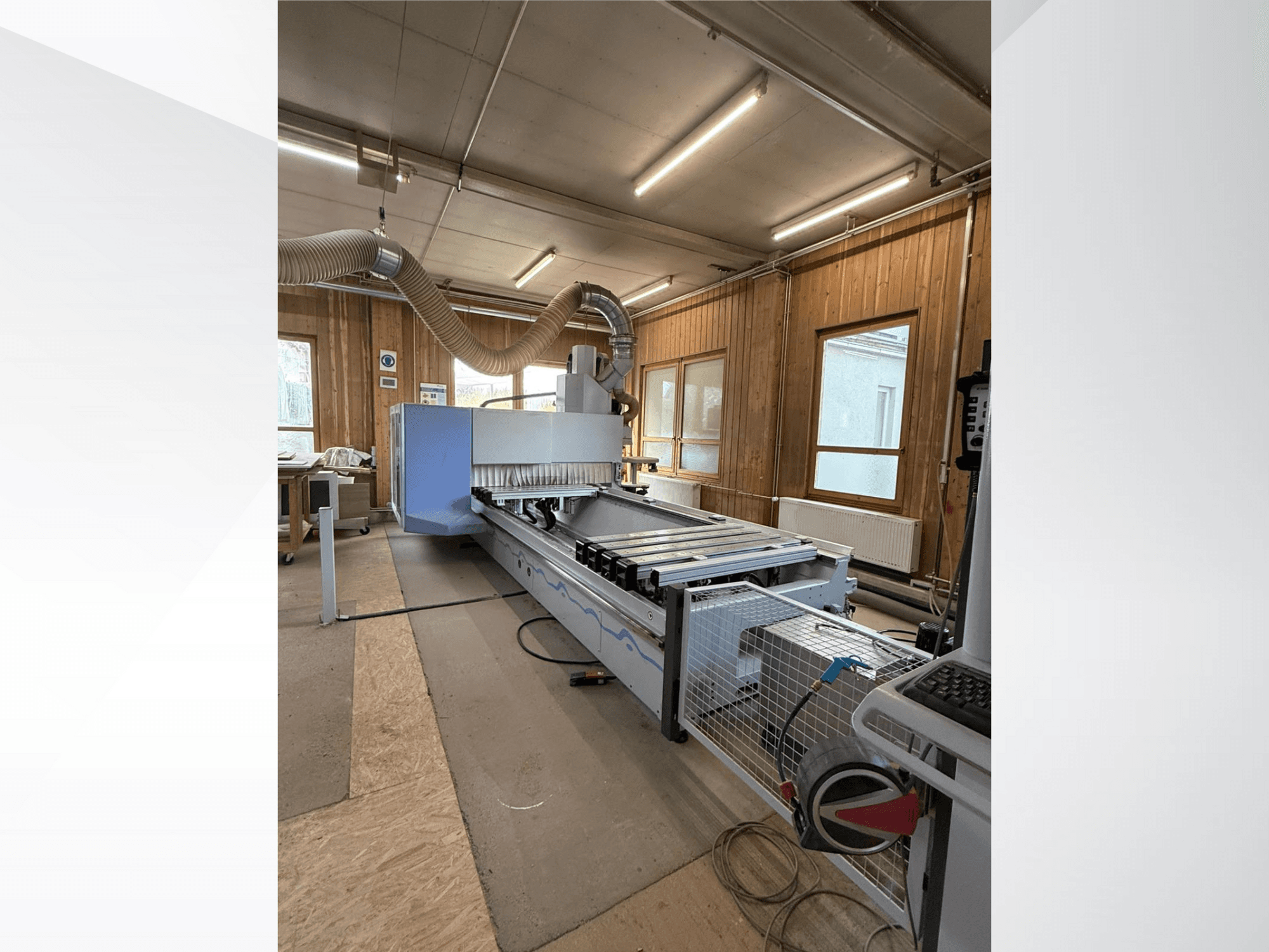 Bir atölyedeki CNC freze makinesi, yandan görünüm, büyük mavi gövde, bağlı bantlı konveyör ve görünür kontrol paneli.