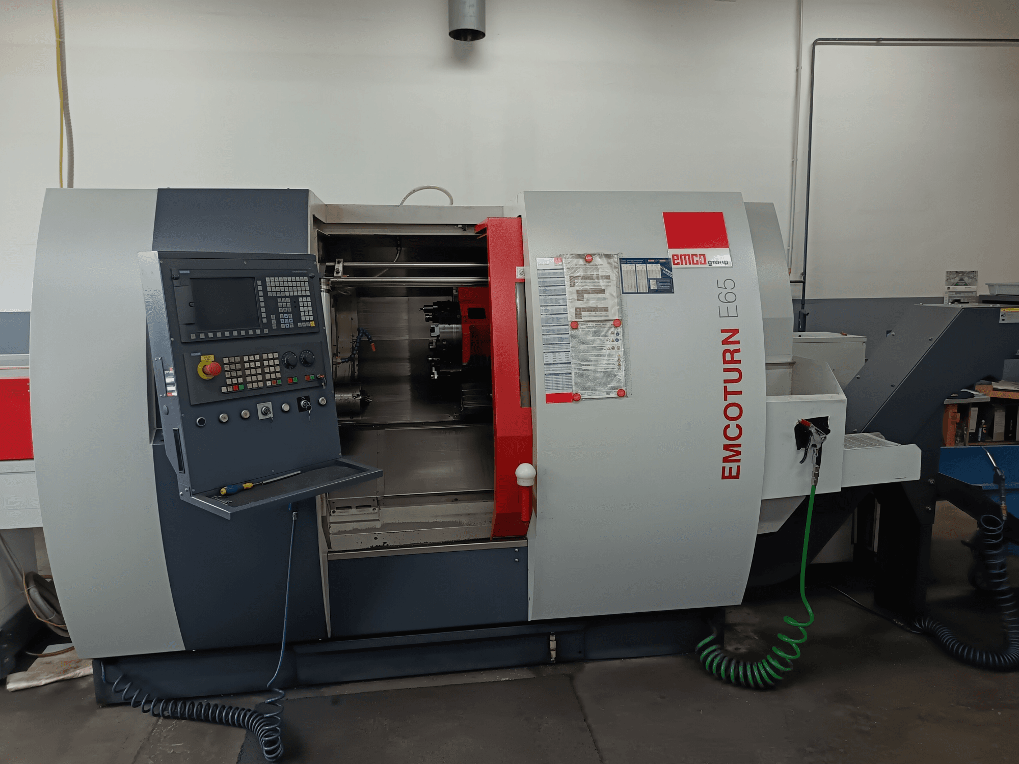 EMCO EMCOTURN E65 torna değirmen merkezi, kontrol panelini, iç mekanizmayı ve atölye ortamındaki özellikleri gösteren önden görünüm.