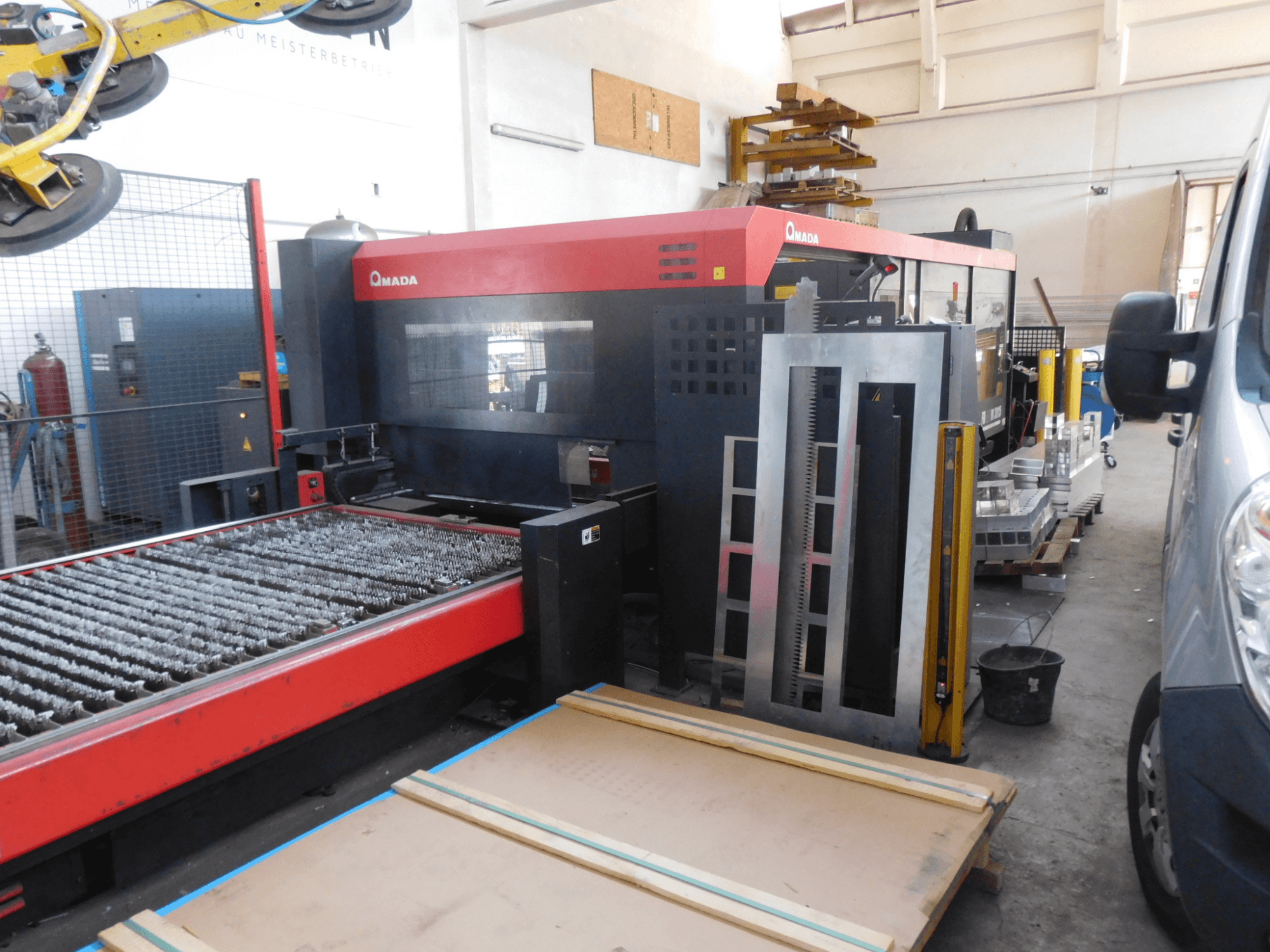 AMADA FO-3015 II RI CO2 lazer kesim makinesinin önden görünümü, kesim yatağı ve çevresindeki çalışma alanı.