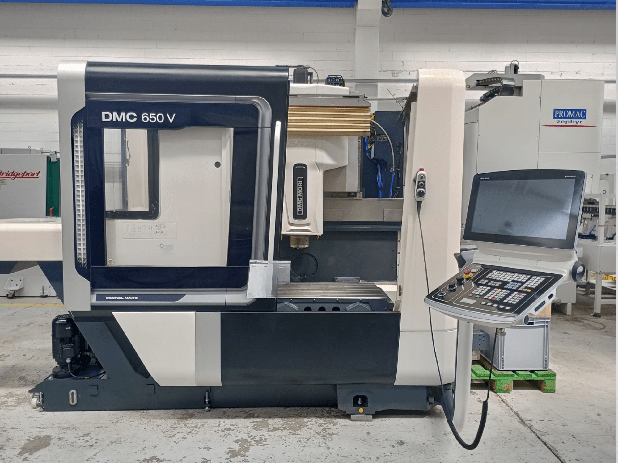 Decker Maho DMC 650 V CNC makinesinin yandan görünümü, düğmeli bir kontrol paneli ve bir ekran, endüstriyel ortamda.