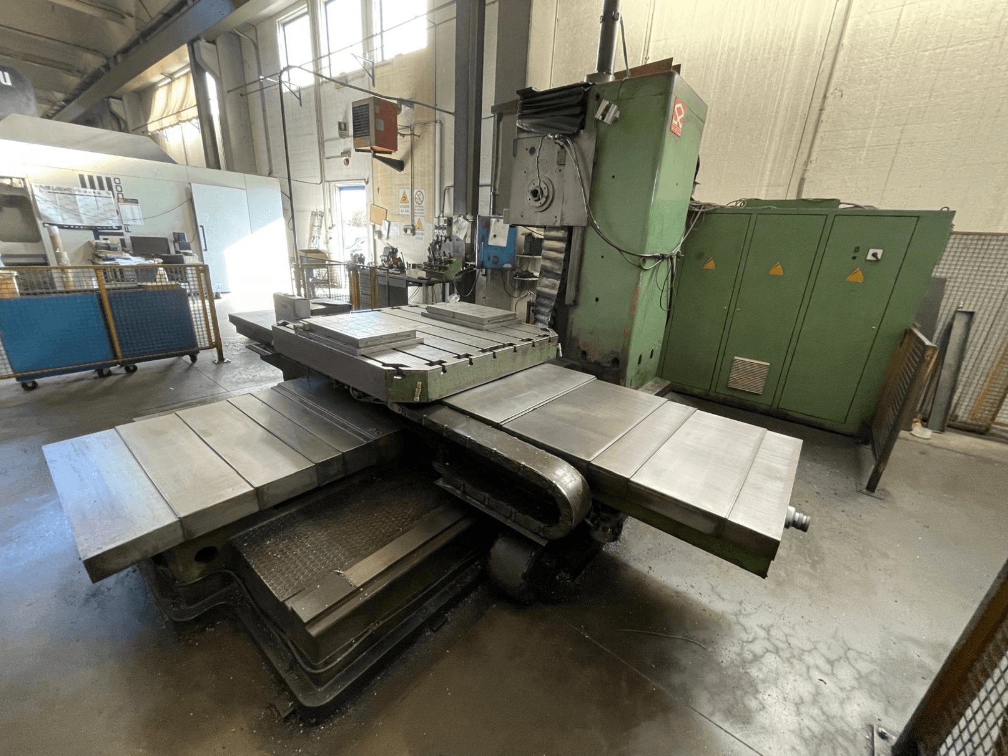 Yeşil gövdeli büyük endüstriyel freze makinesi, yandan görünüm, birden fazla düz yüzey ve arka planda depolama dolapları.