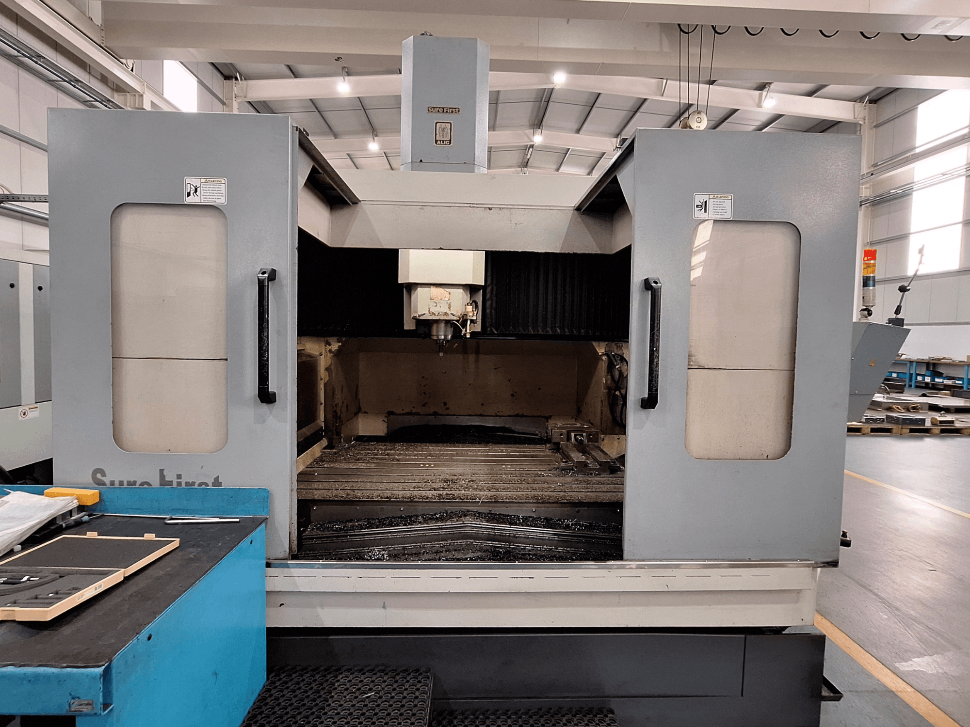 Dikey işleme merkezi Sure First QM-1836, takım kafasını ve boş çalışma alanını gösteren önden görünüm, modern endüstriyel ortam.