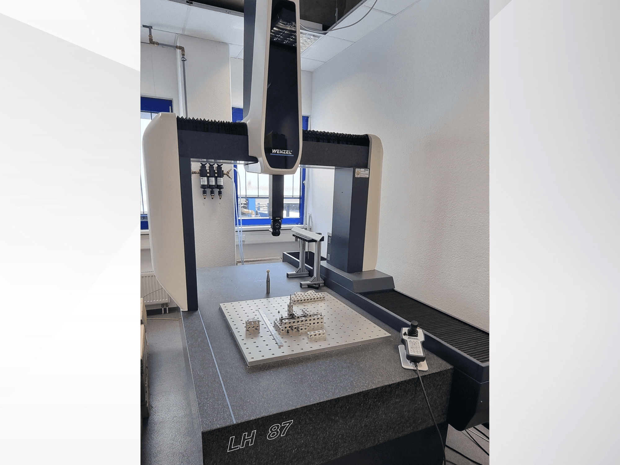 Bir laboratuvarda bulunan Wenzel LH 87 CMM; hassas bir yüzey plakası üzerinde ölçüm probu bulunurken, dijital kontrol ünitesi de görülebilen önden görünüm.