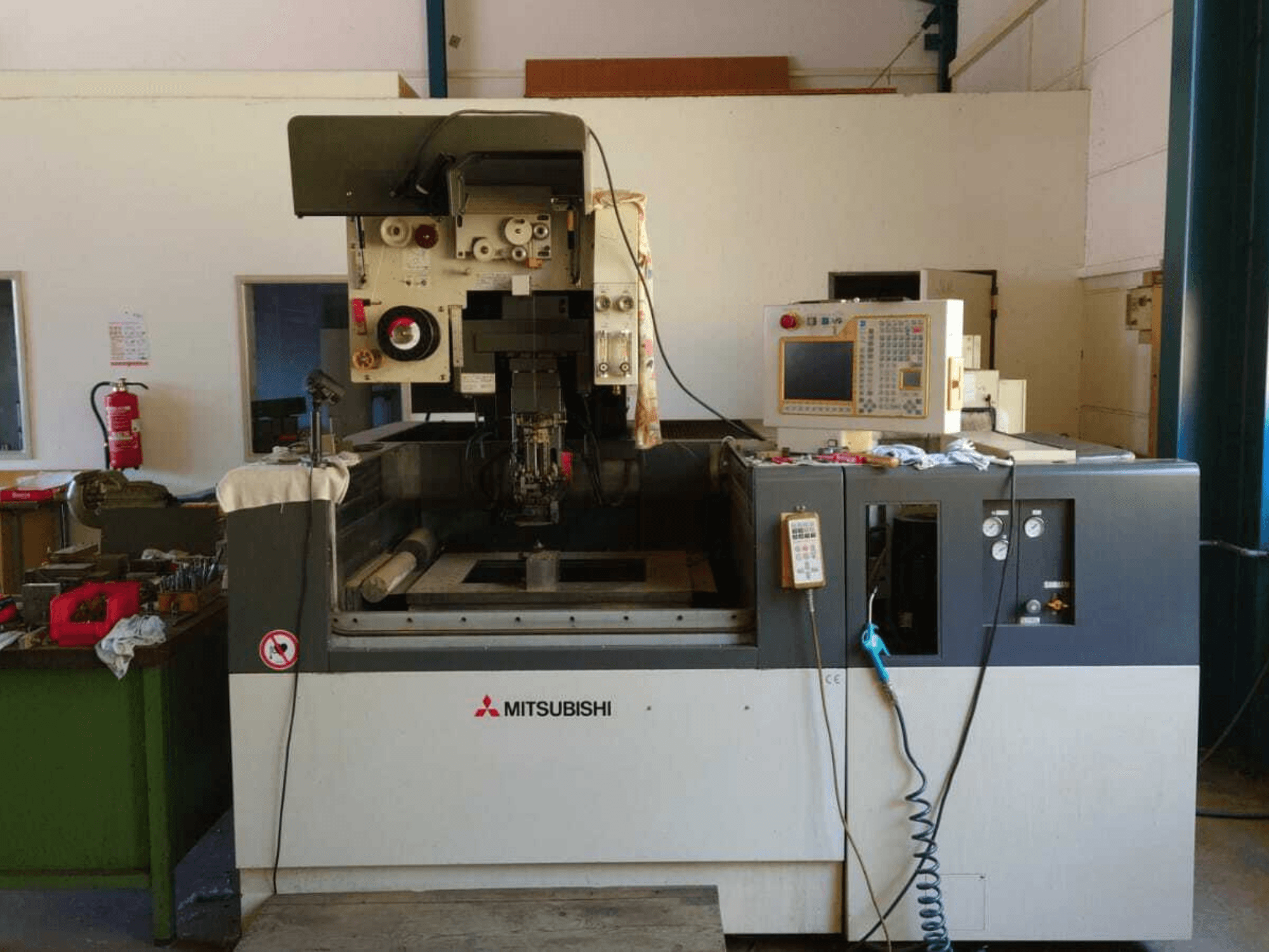 Mitsubishi FA20 Tel Elektrikli Kesişimli Makine’nin ön görünümü; kontrol paneli, çalışma alanı ve güvenlik işaretleri görülebilir.