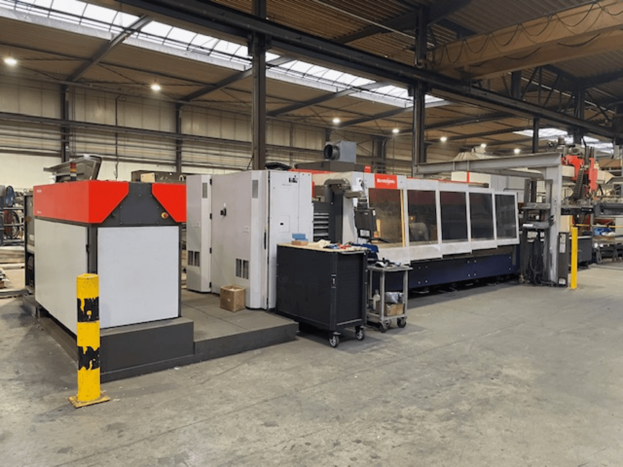 Bystronic BySpeed 3015 CO2 lazer kesim makinesi, bir atölyede yandan görünüm, farklı kırmızı ve gri tasarım öğeleri.