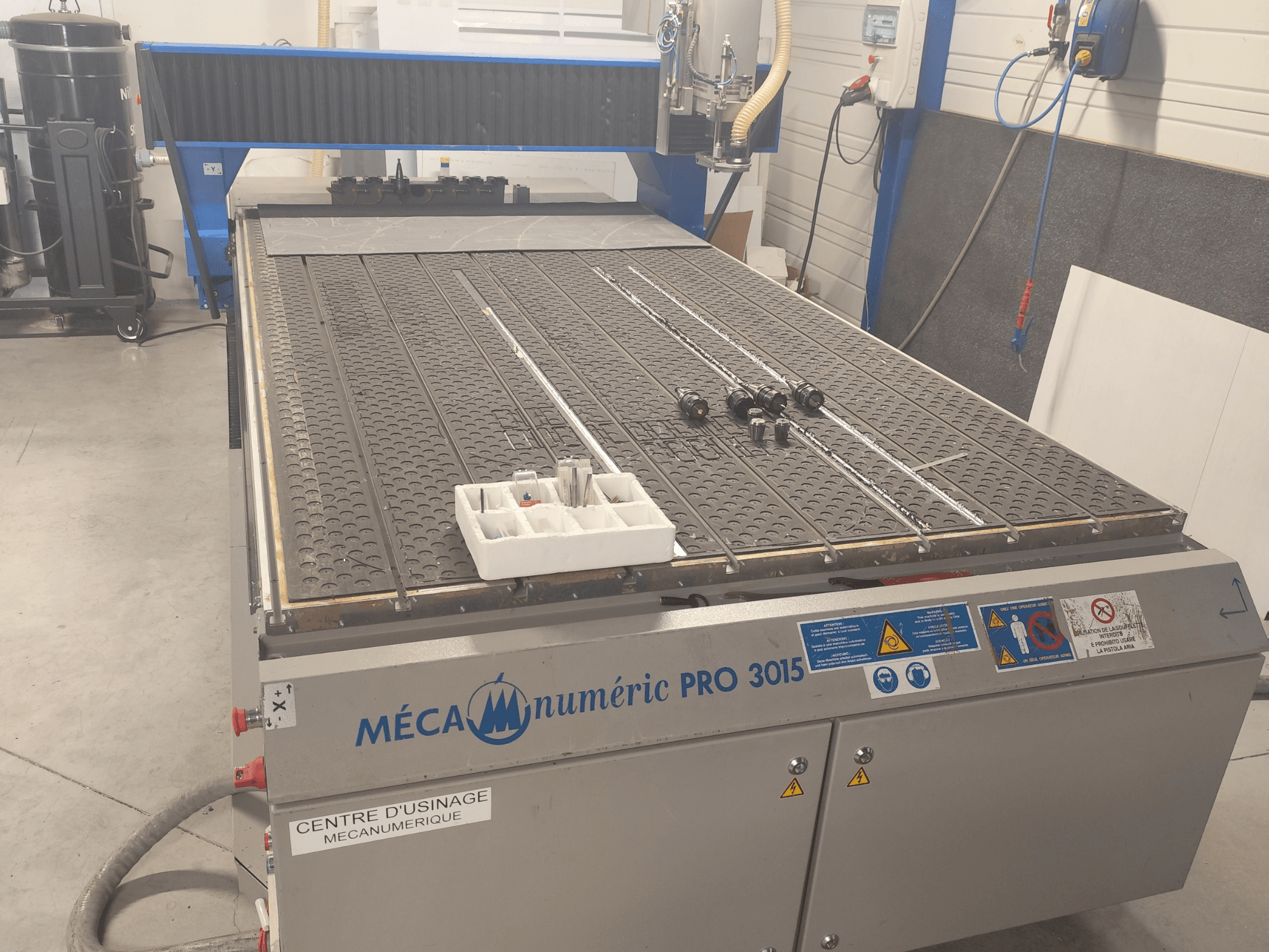 MECANUMERIC Pro 3015 CNC Router’ın önden görünümü; ayrıntılı kesim yatağı, kontrol paneli ve masanın üzerindeki aksesuarlar gösterilmektedir.