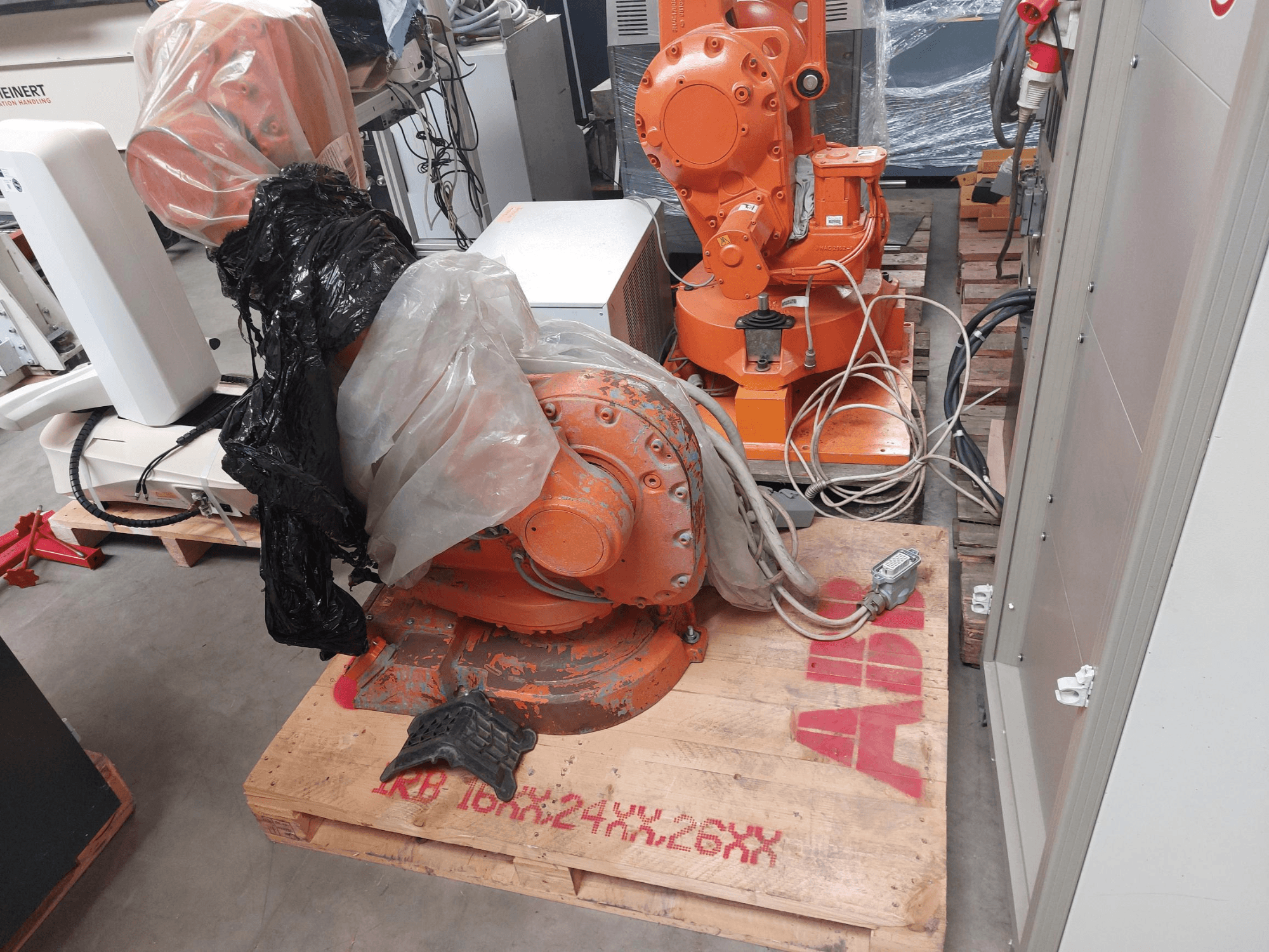 ABB IRB 1600 M2004 robot kolu kısmen plastikle kaplı, önden bakıldığında kablolar ve ek makineler yakındadır.