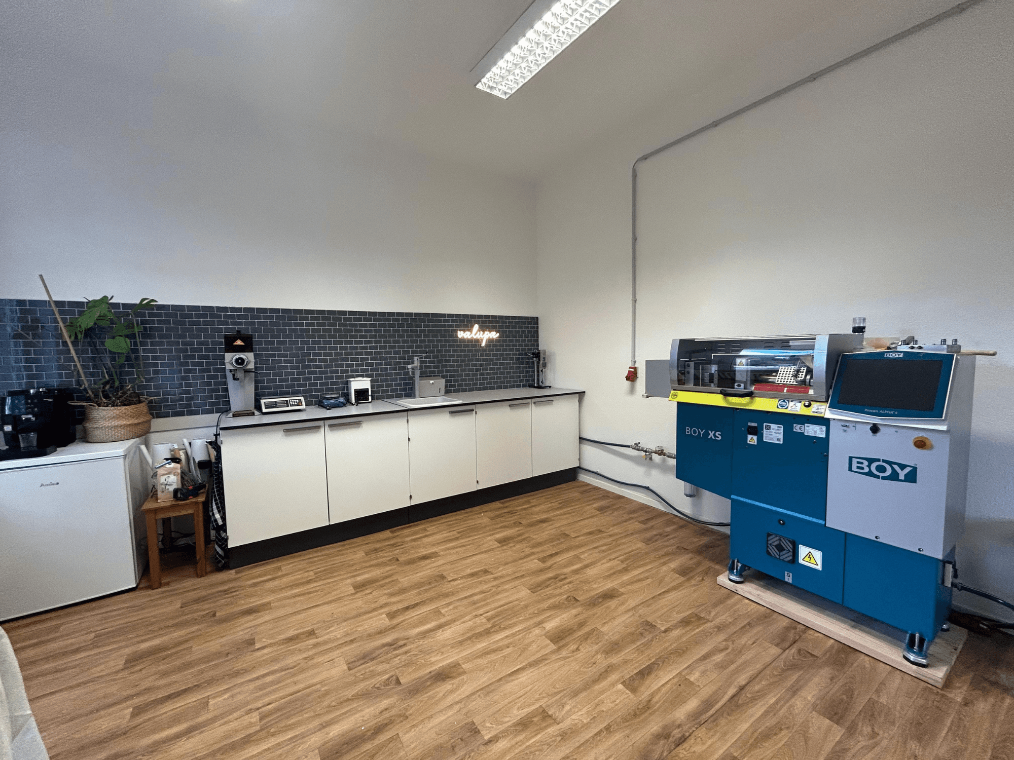 Hidrolik enjeksiyon kalıplama makinesi BOY XS 161, önden görünüm, aletler ve ahşap döşeme ile modern bir mutfak ortamında.