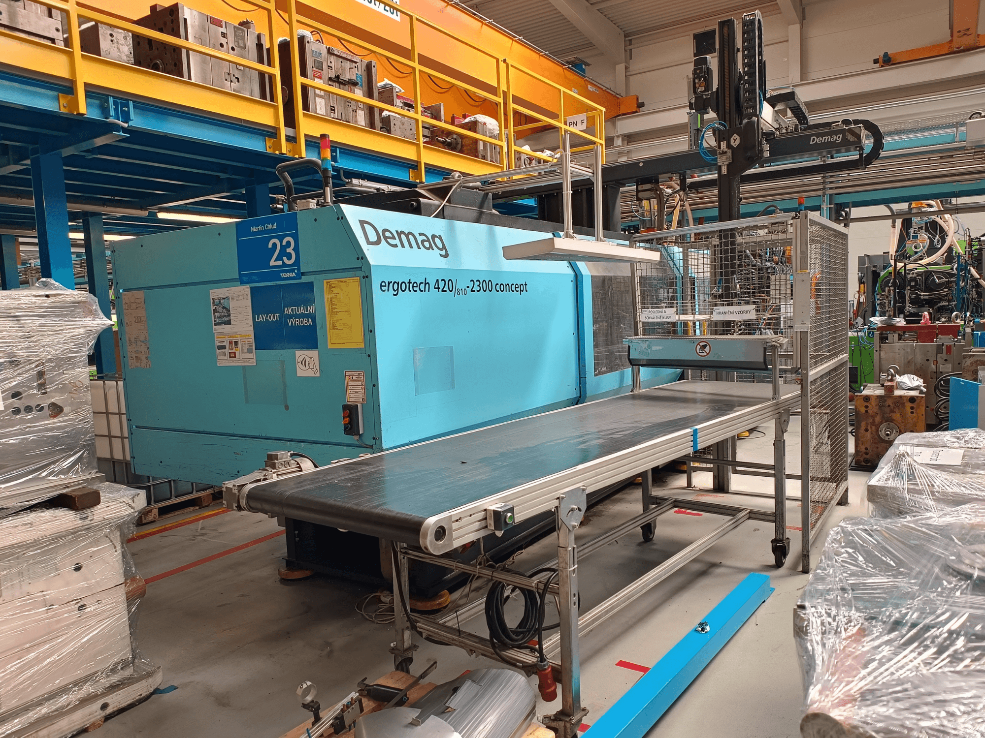 Demag ergotech 420/810 - 2300 hidrolik enjeksiyon kalıplama makinesinin yandan görünümü, konveyör ve güvenlik muhafazası.