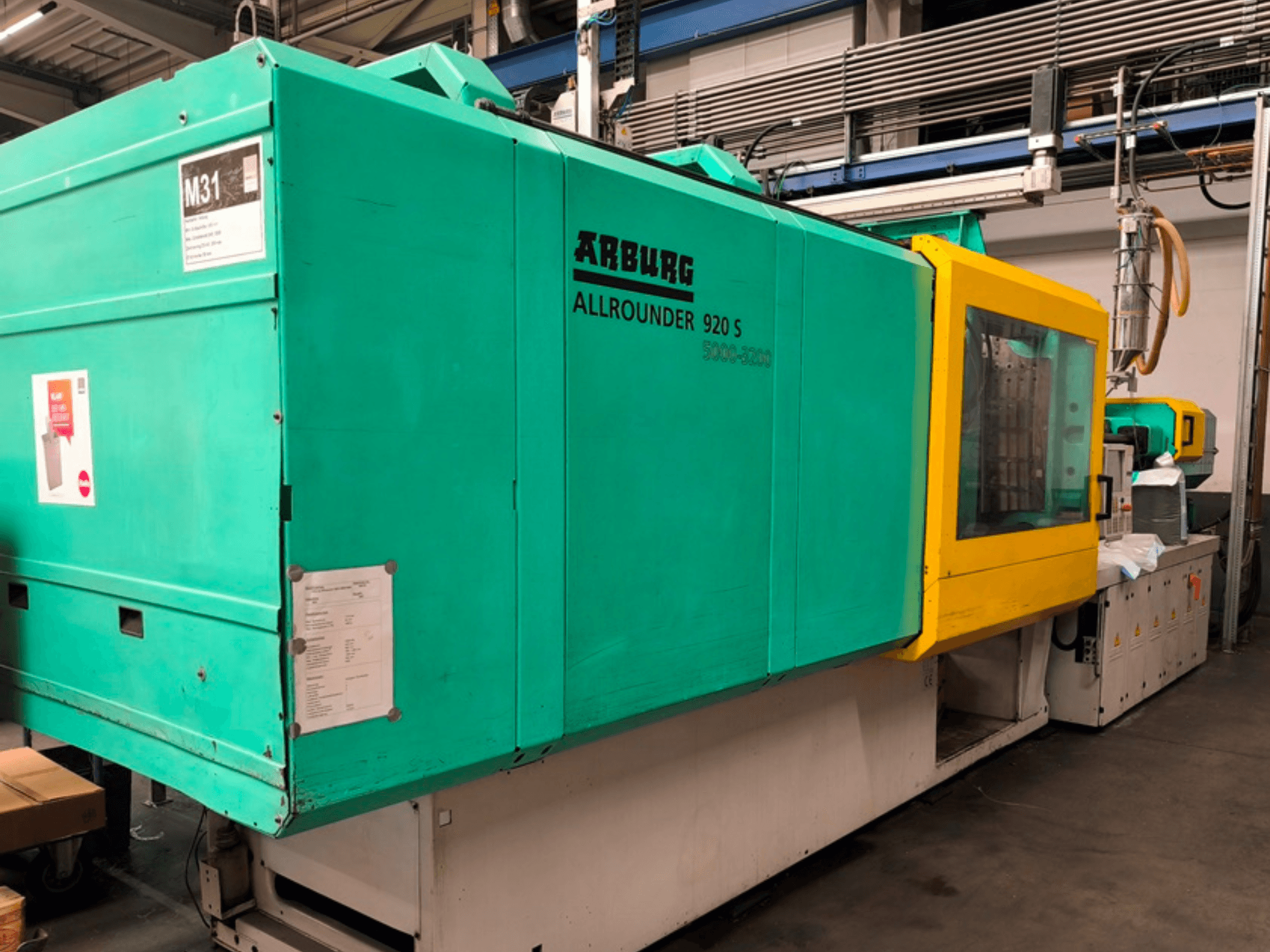 Su mavisi ve sarı renkte Arburg Allrounder 920 S enjeksiyon kalıplama makinesi, kontrol paneli ve bileşenleri gösteren yandan görünüm.