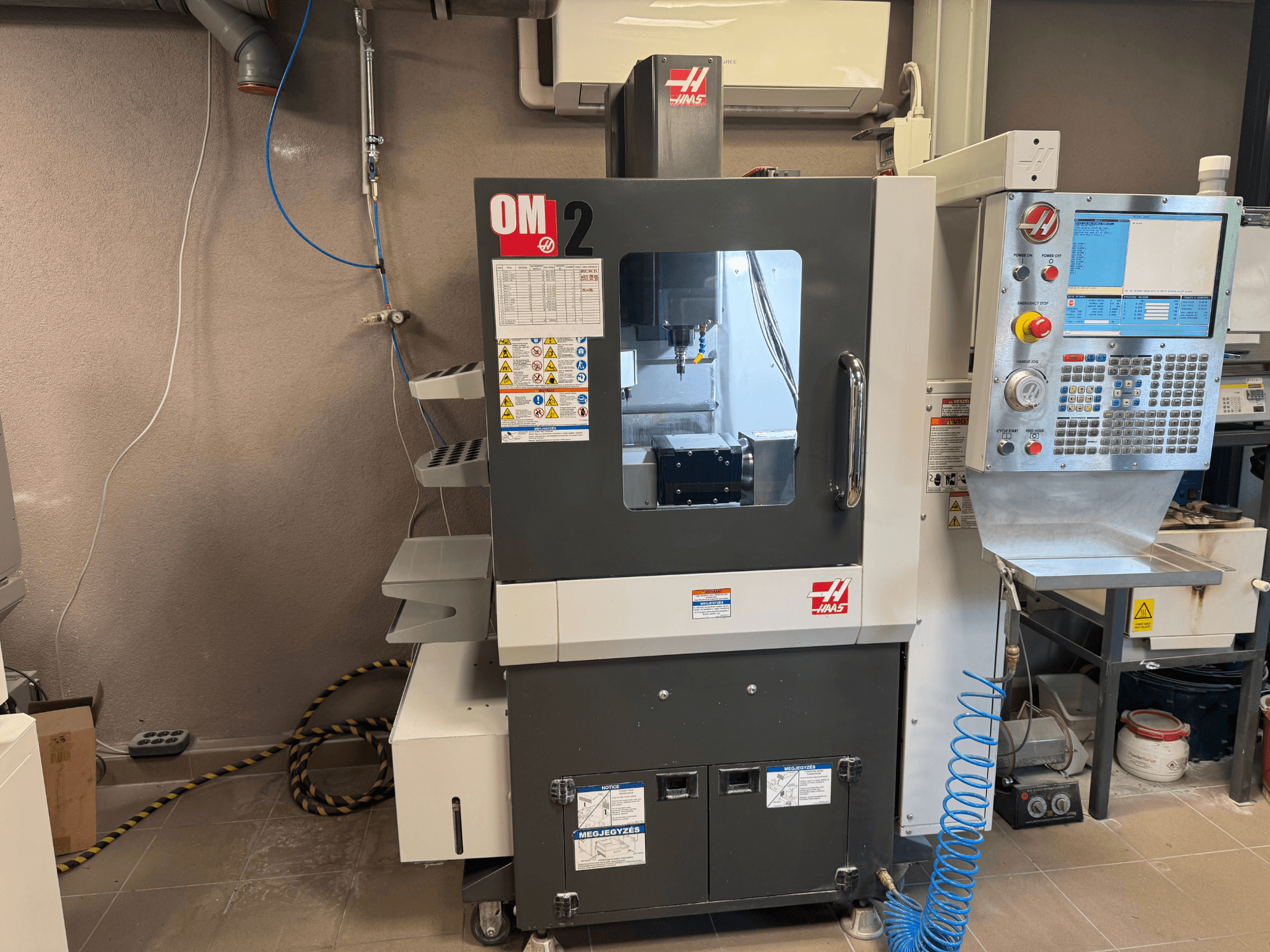 Haas OM-2 CNC makinesi, önden görünüm, kontrol paneli, iş mili ve güvenlik etiketleri, bir atölye ortamında ayarlanmıştır.