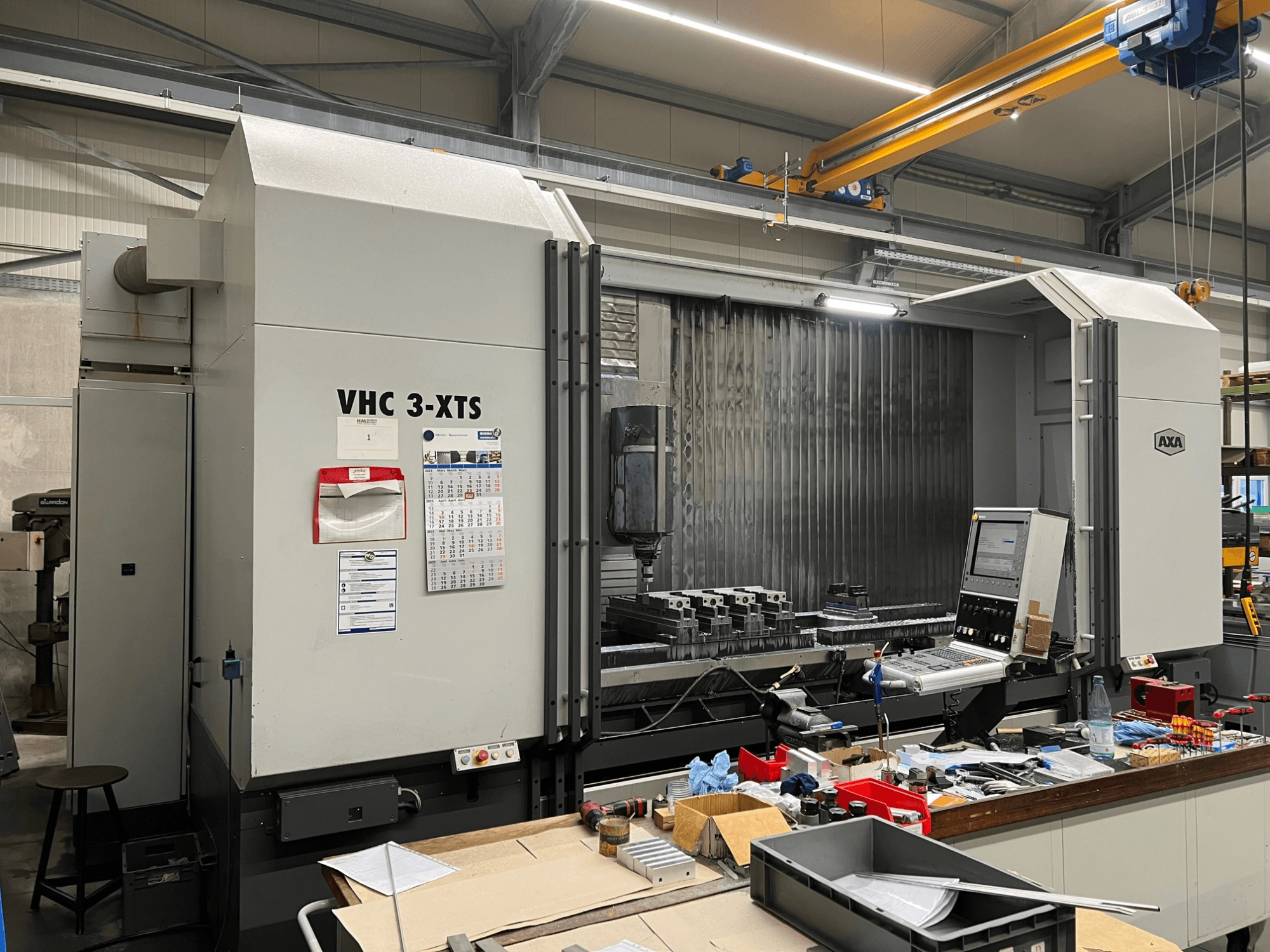 AXA VHC 3-XTS CNC makinesi yandan görünümde, kontrol paneli ve çalışma alanı aletler ve bileşenlerle dolu.