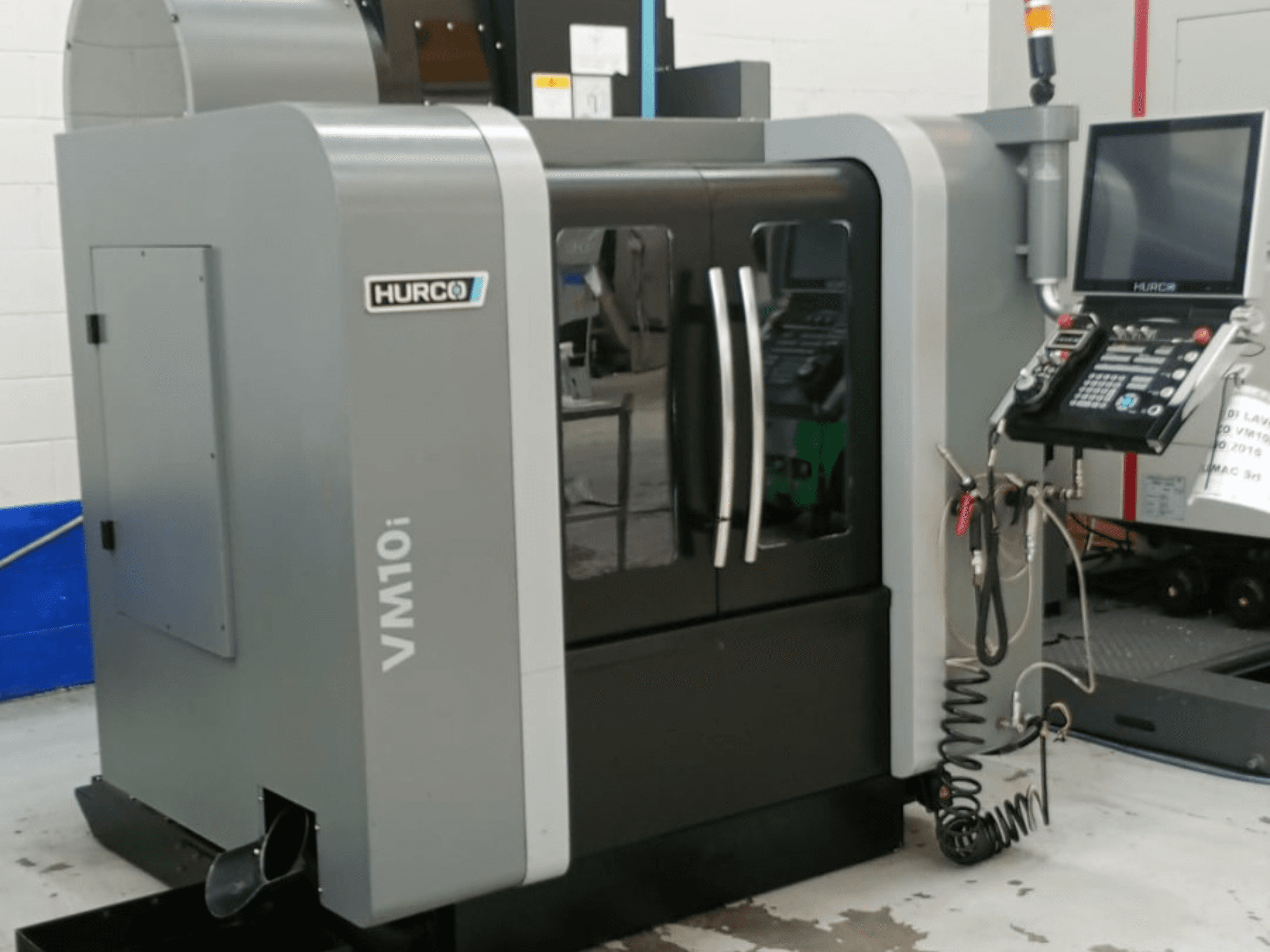 Hurco VM10i dikey işleme merkezinin yandan görünümü; çift kapı, kontrol paneli ve çalışma sırasında görünen kablolar.