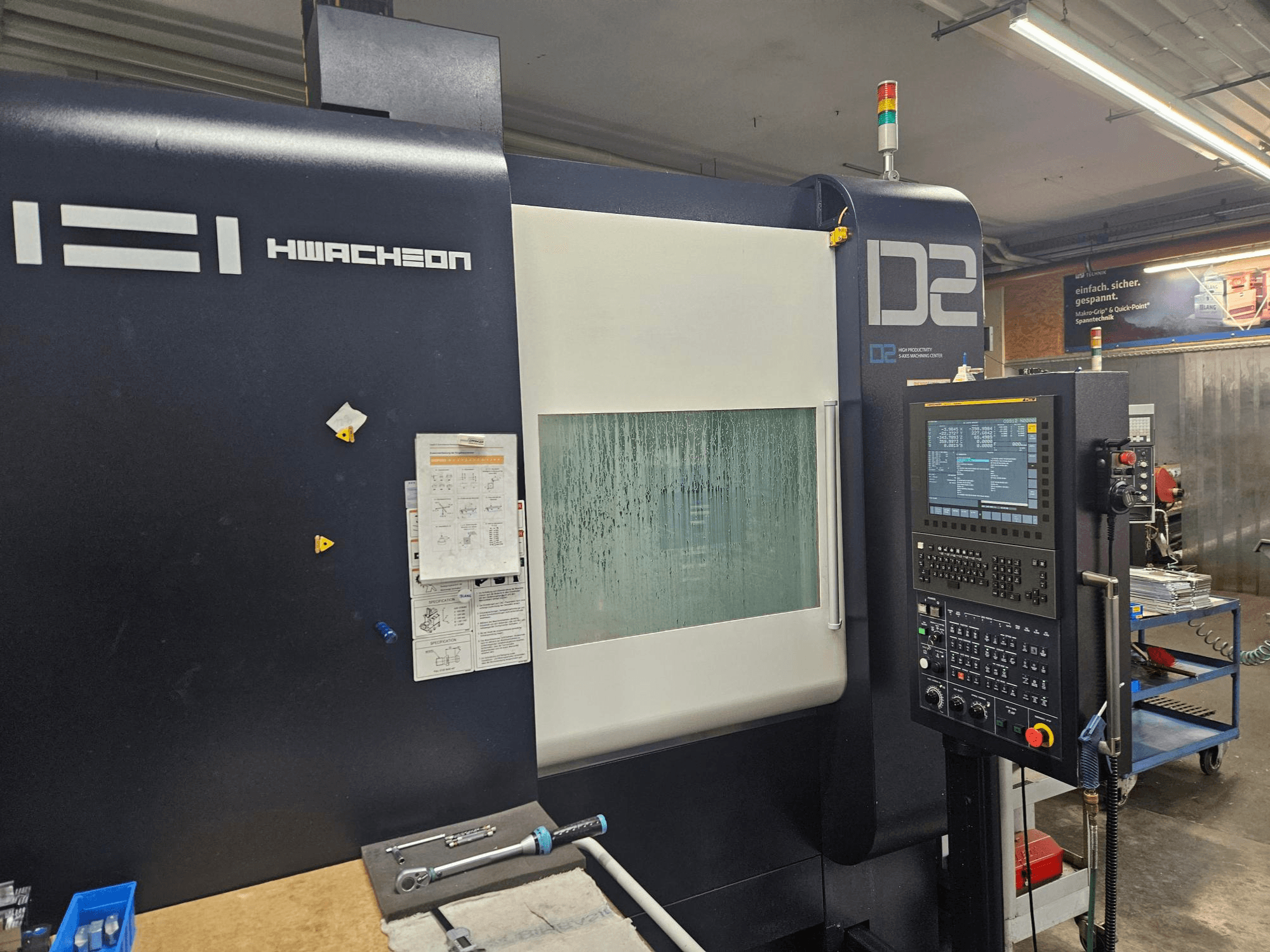 HWACHEON D2-5AX 12k dikey işleme merkezi; kontrol paneli ve buğulanmış gözetleme penceresini gösteren önden görünüm.