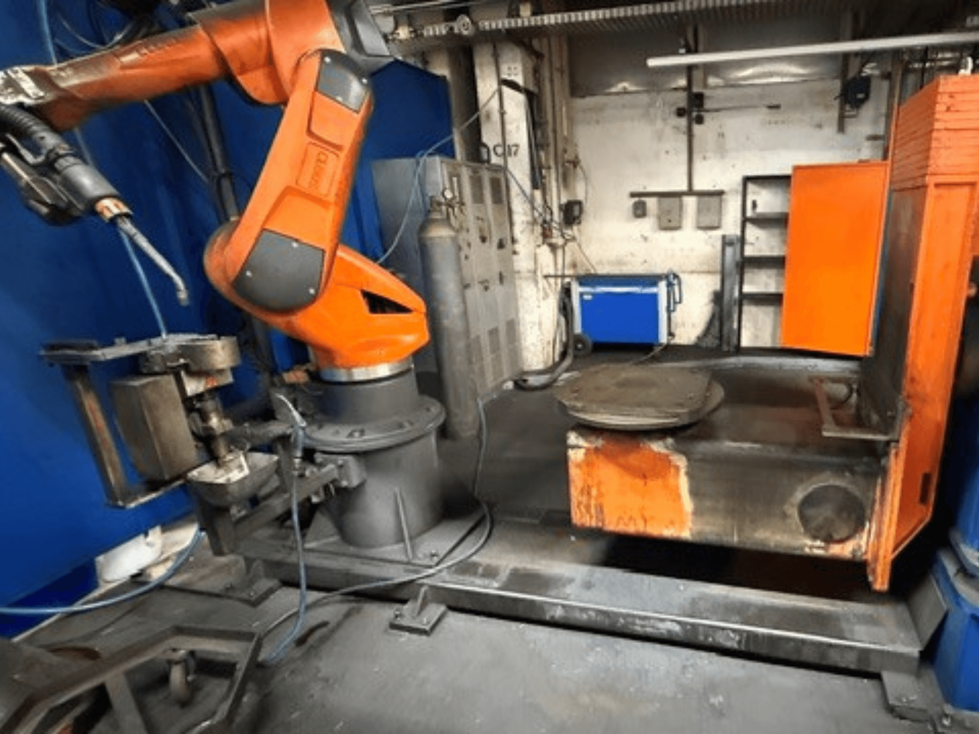 CLOOS C50 kaynak robotunun önden görünümü; turuncu renkli bir robot kolu ve metal bir çalışma masası bulunmaktadır.