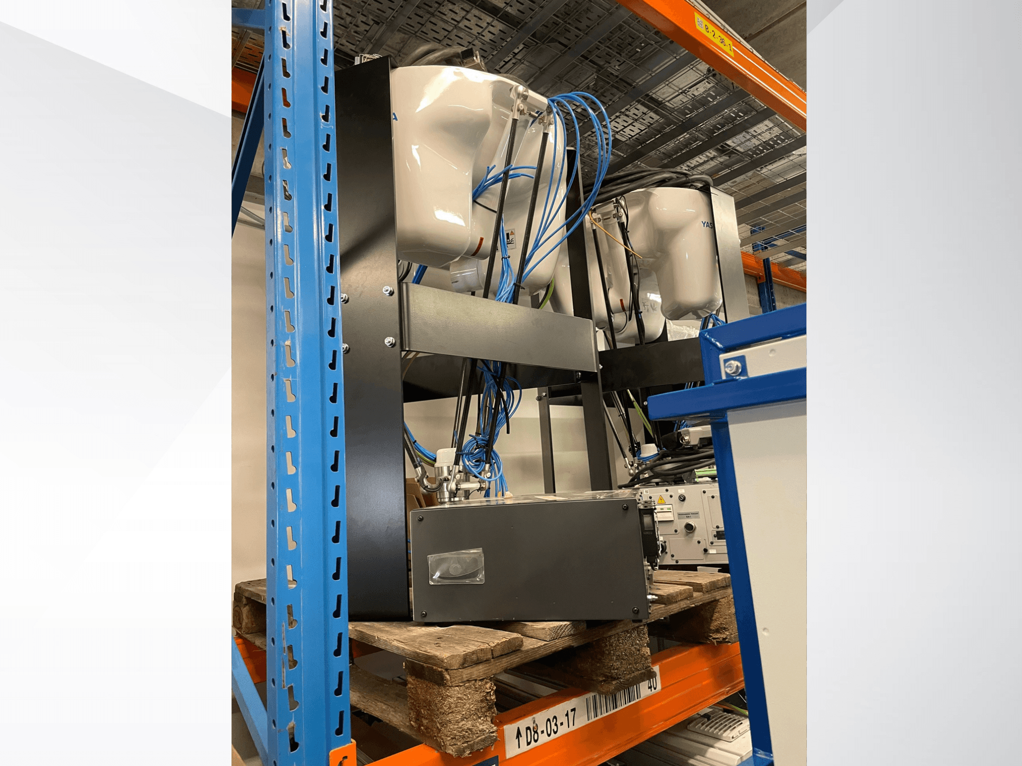 Yaskawa Motoman MPP3H robot kolu, yandan görünümde; kablolama ve bileşenler bir depolama rafında görülebilir.
