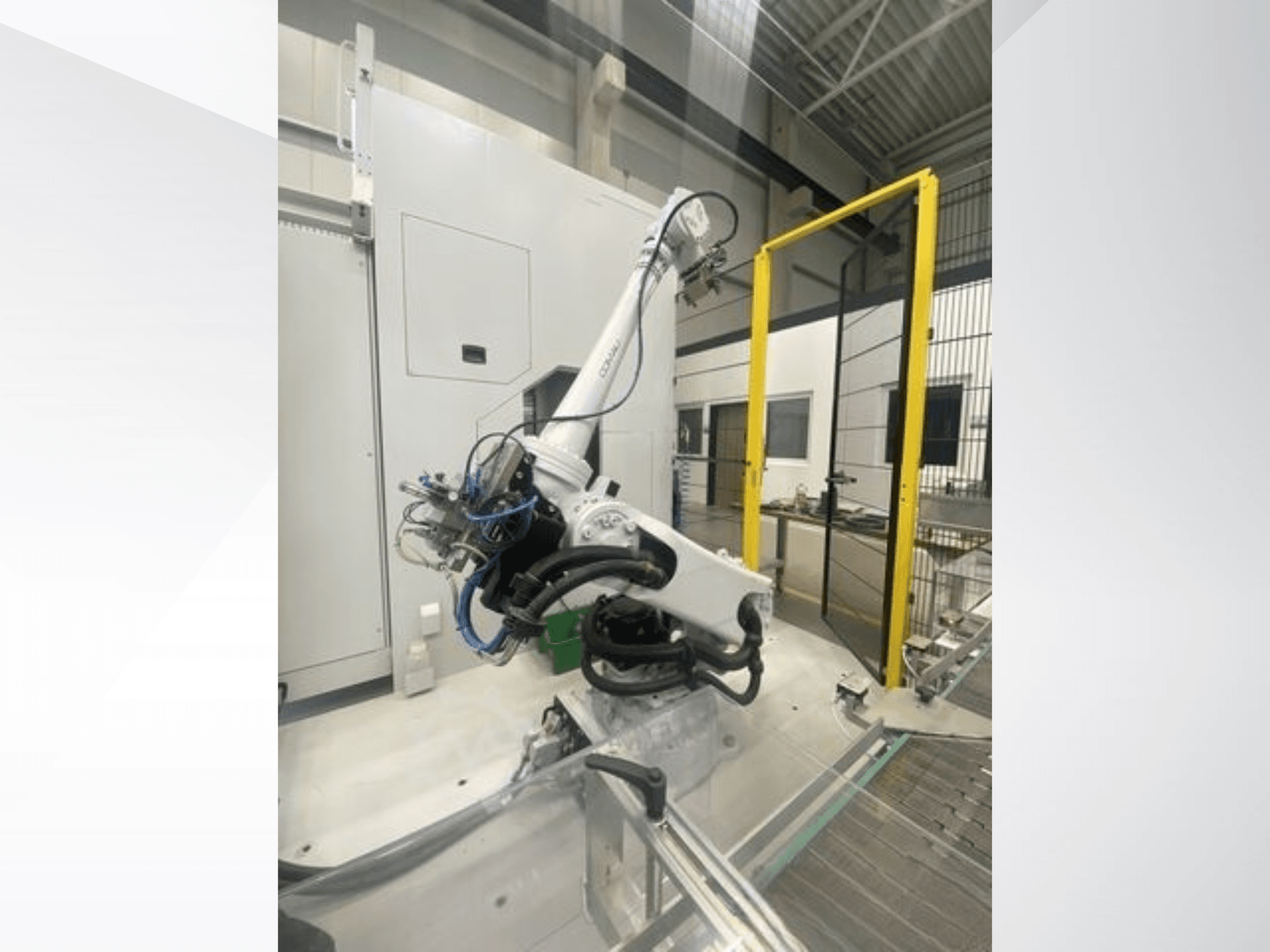 COMAU Smart NJ 40-2.5 robot kolu yandan görünümde, fabrika ortamında kablolar ve sarı bir güvenlik kapısı içerir.