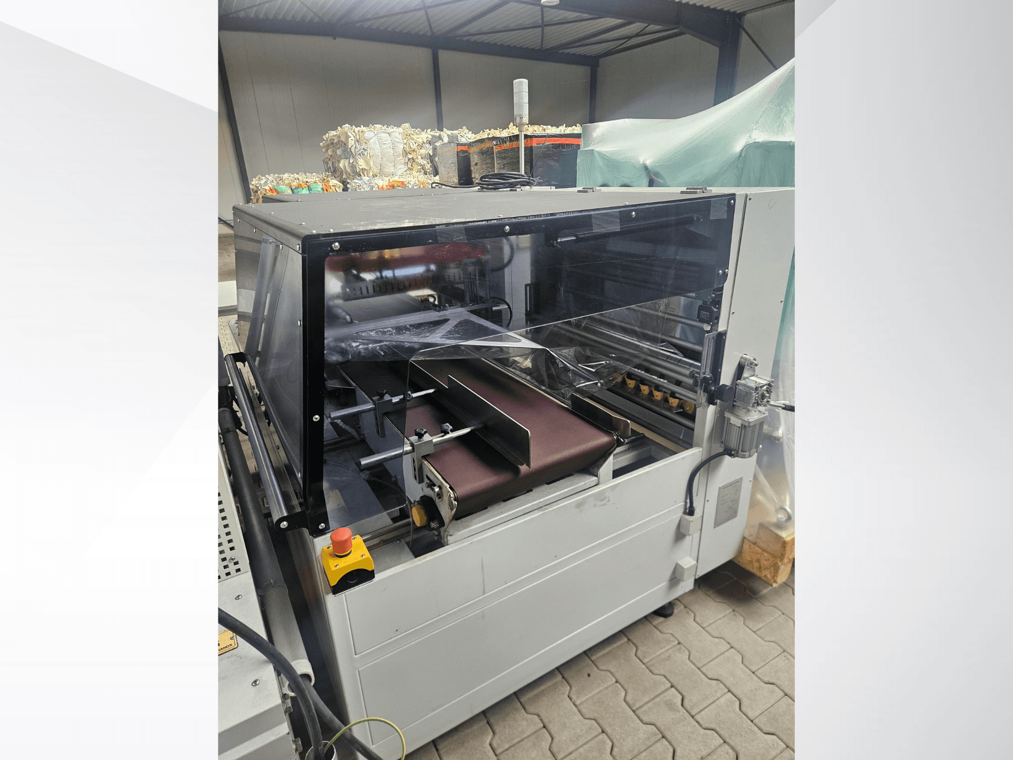 AMTEC Speed Shrink 40 PRO makinesi, önden görünüm; şeffaf bir güvenlik kapağı ve konveyör bandına sahip plastik işleme mekanizması görülmektedir.
