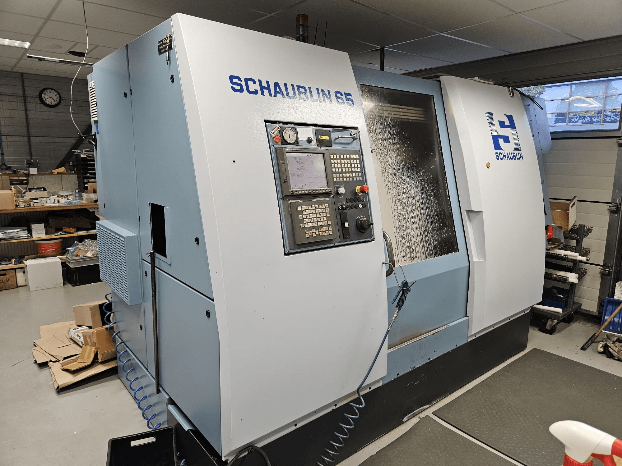 SCHAUBLIN 65 CNC makinesi, yandan görünüm, kontrol paneli, mavi ve gri gövde ve görünür soğutma sistemi.