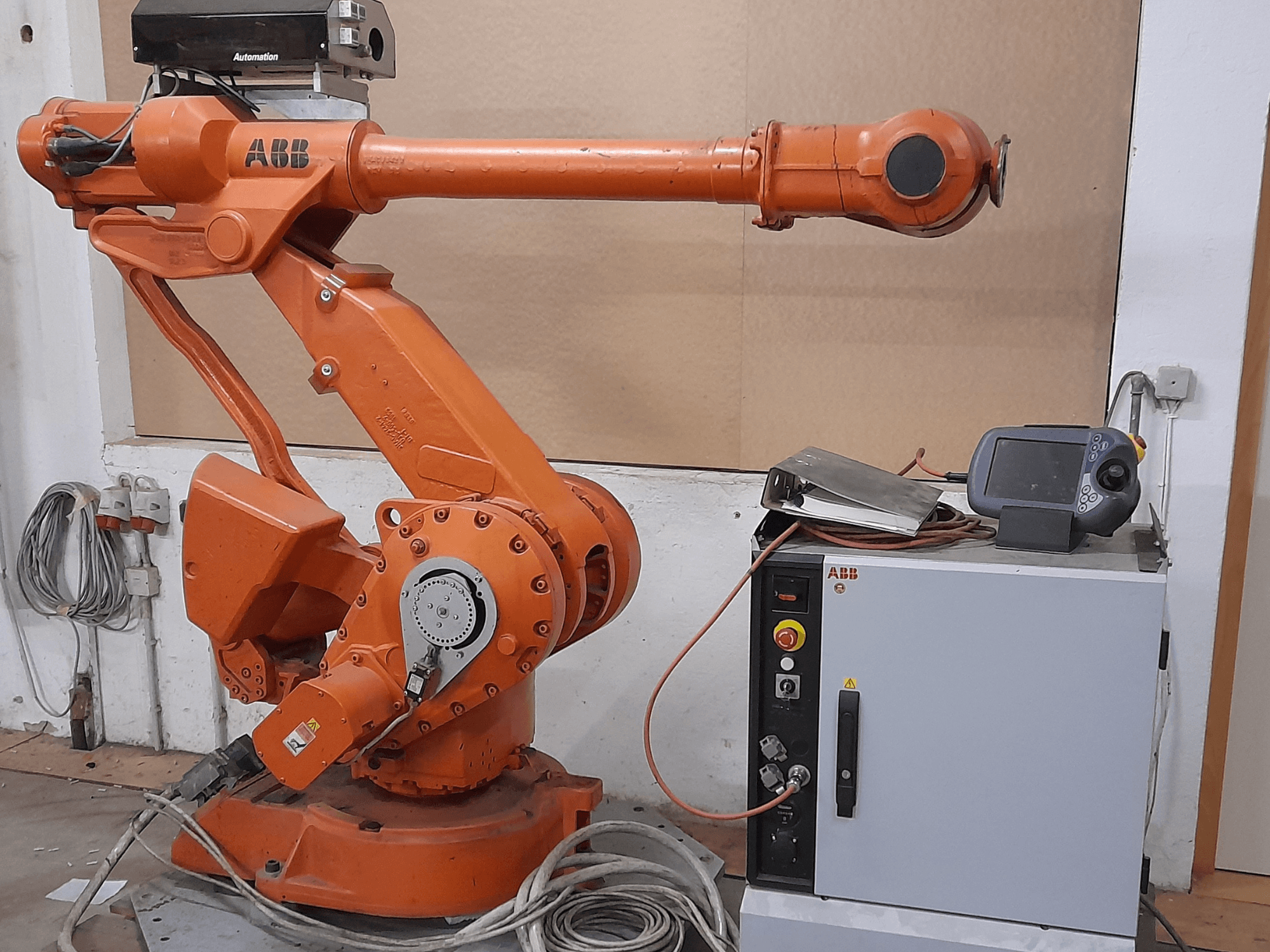 Kontrol panelli turuncu ABB robot kolu, önden görünüm, kablolar ve otomasyon ekipmanı sergileniyor.