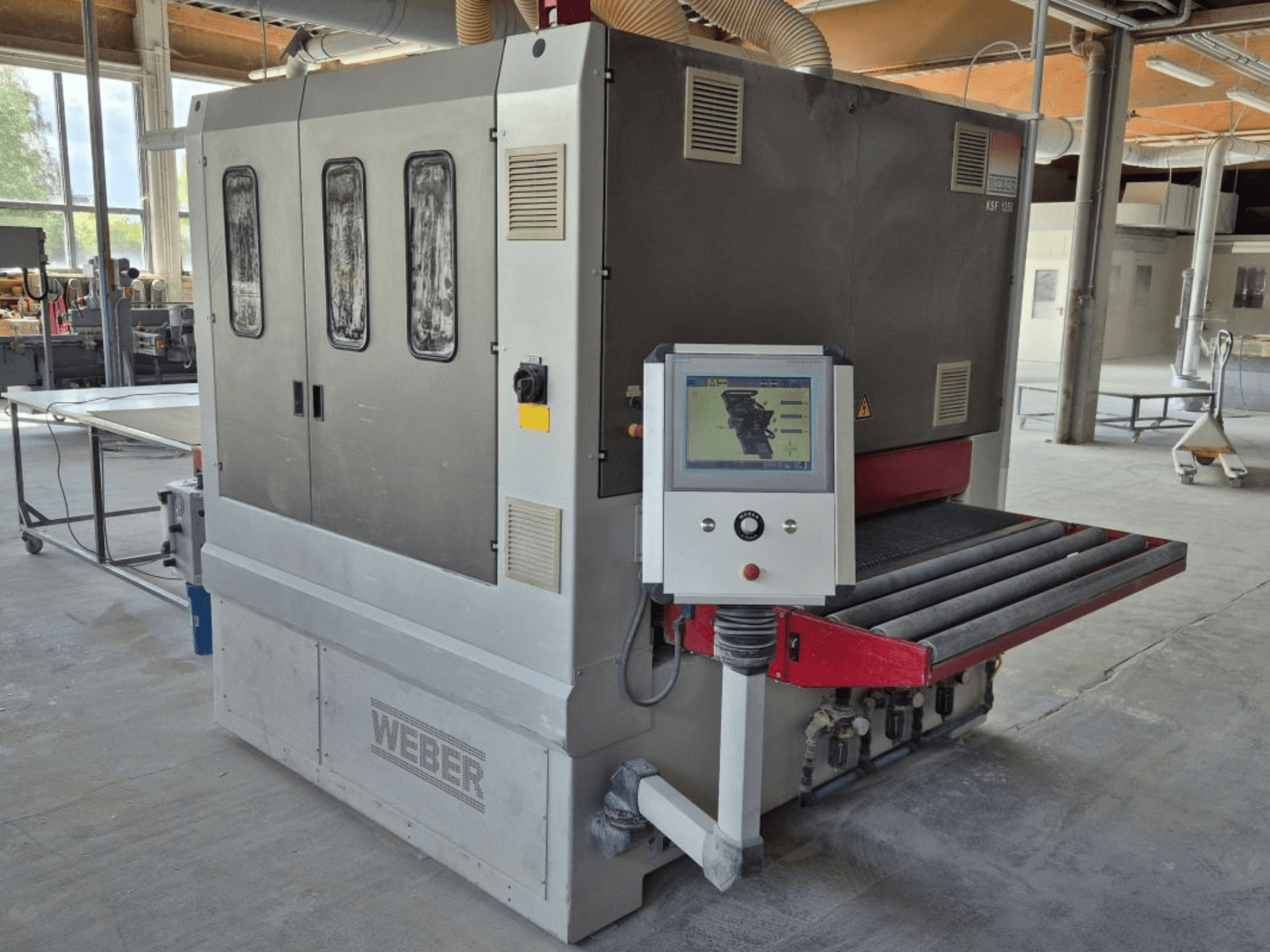 WEBER KSF-3-1350 bant zımpara makinesi, kumandaları, güç panelini ve zımpara konveyörünü gösteren yandan görünüm. Makinelerin göründüğü endüstriyel ortam.