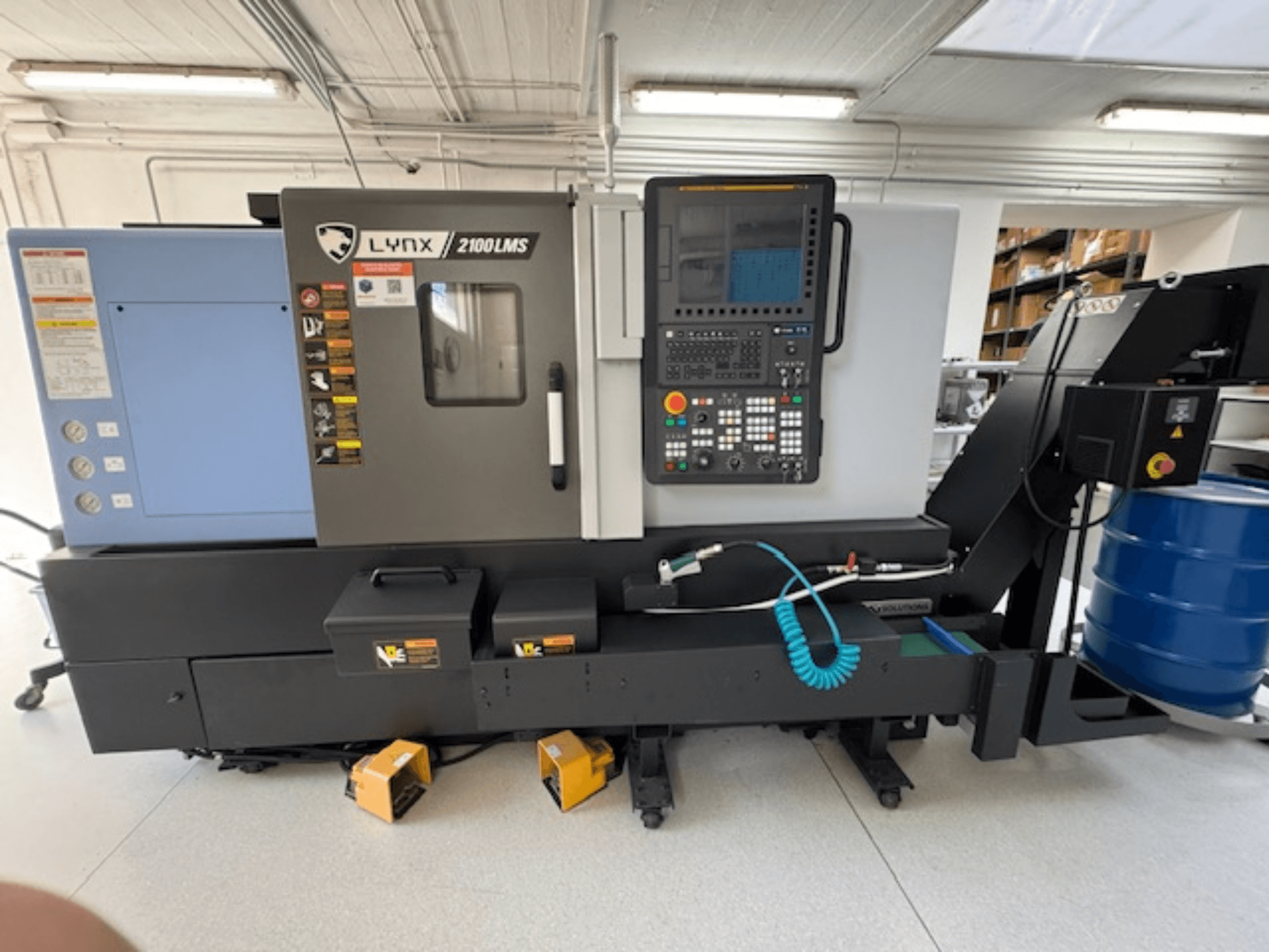 DOOSAN LYNX 2100LMSA yatay tornalama makinesi, önden görünüm, kontrol paneli, soğutma sıvısı hortumu ve saklama kutuları.