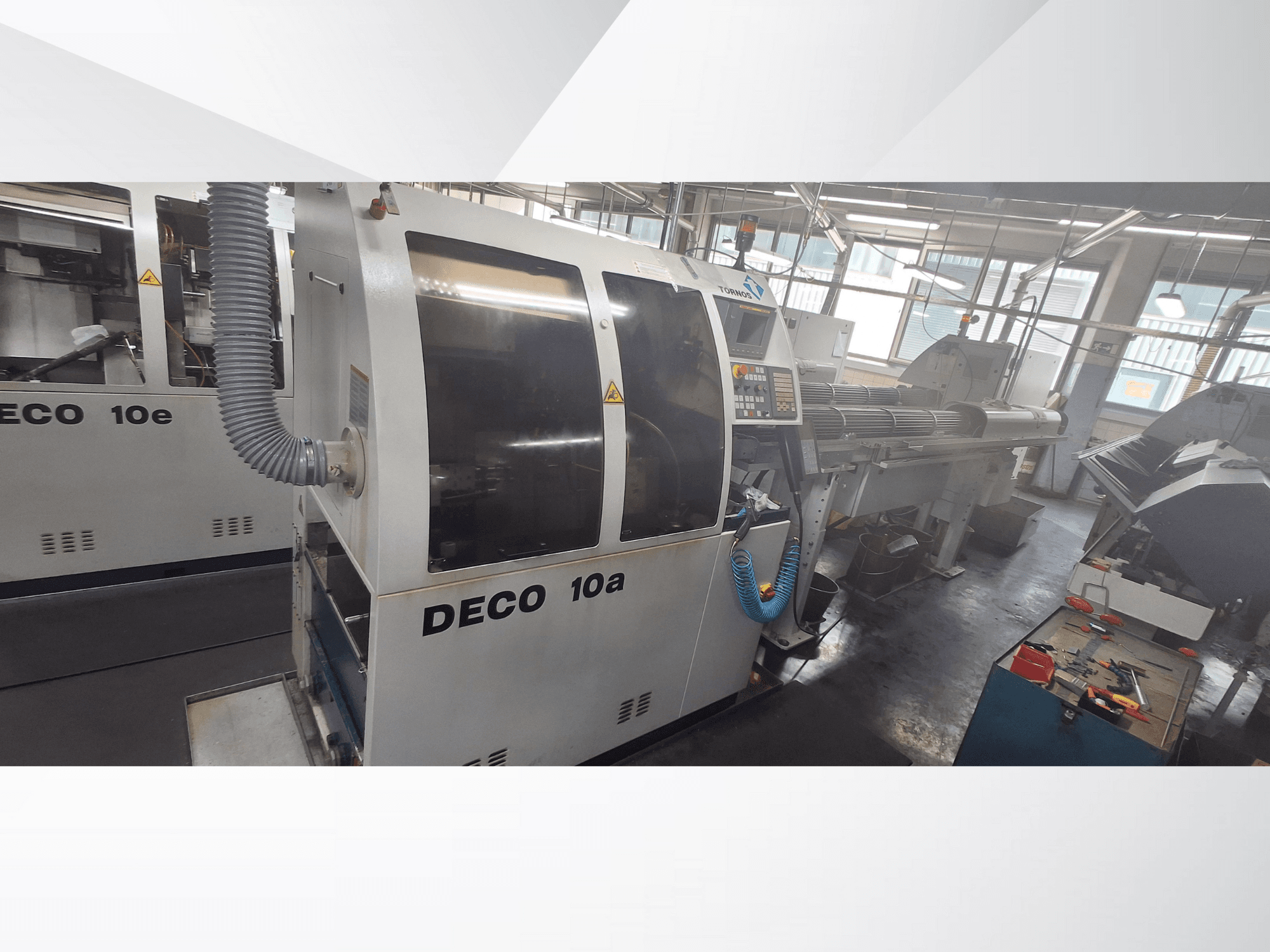 DECO 10a CNC makinesi atölyede, önden görünüm, kontrol paneli ve egzoz sistemini gösteriyor. Sağlam yapı ve hassas aletlere sahiptir.